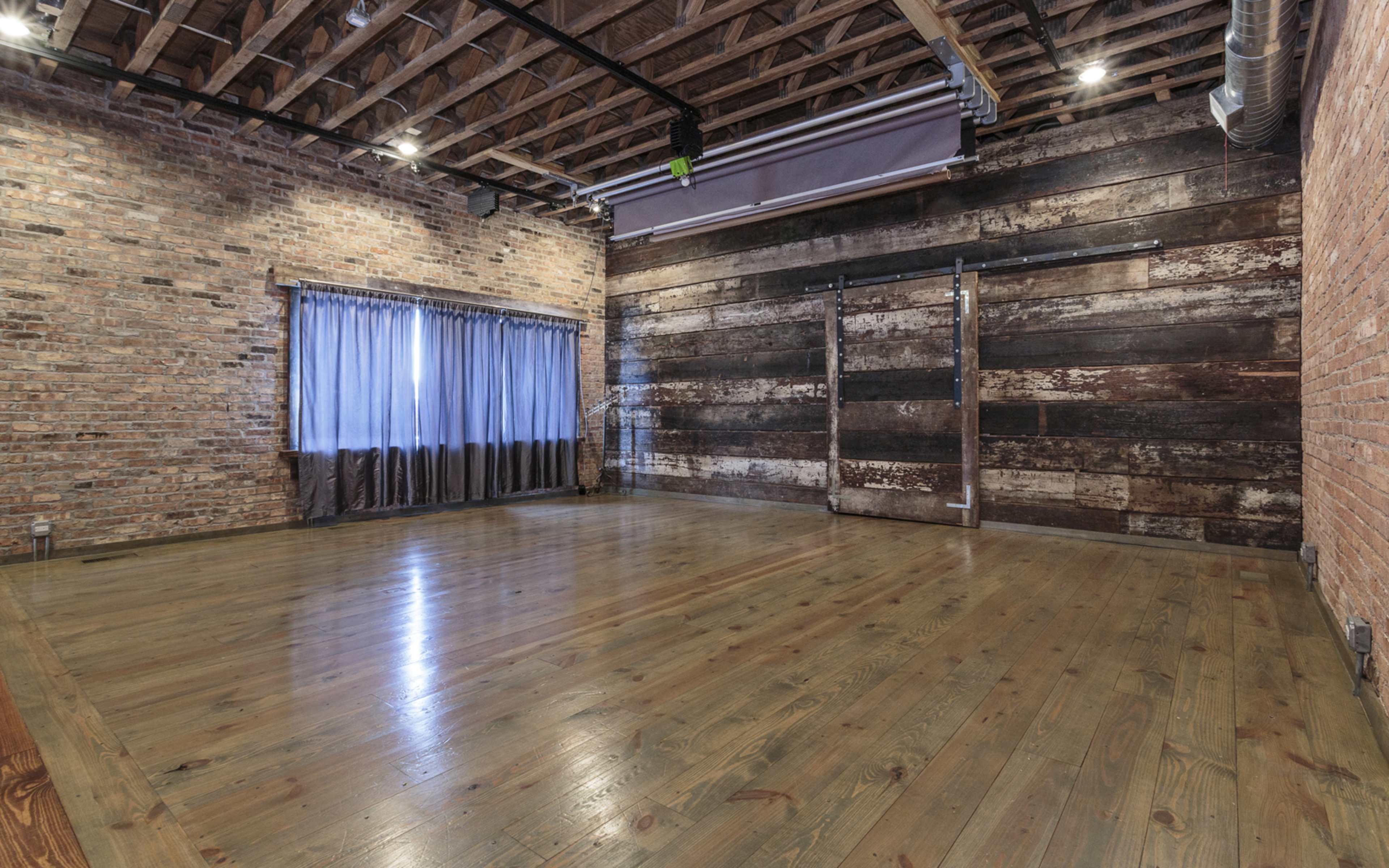 The room features exposed brick walls, wooden flooring, and large windows with curtains, showcasing an industrial design aesthetic.