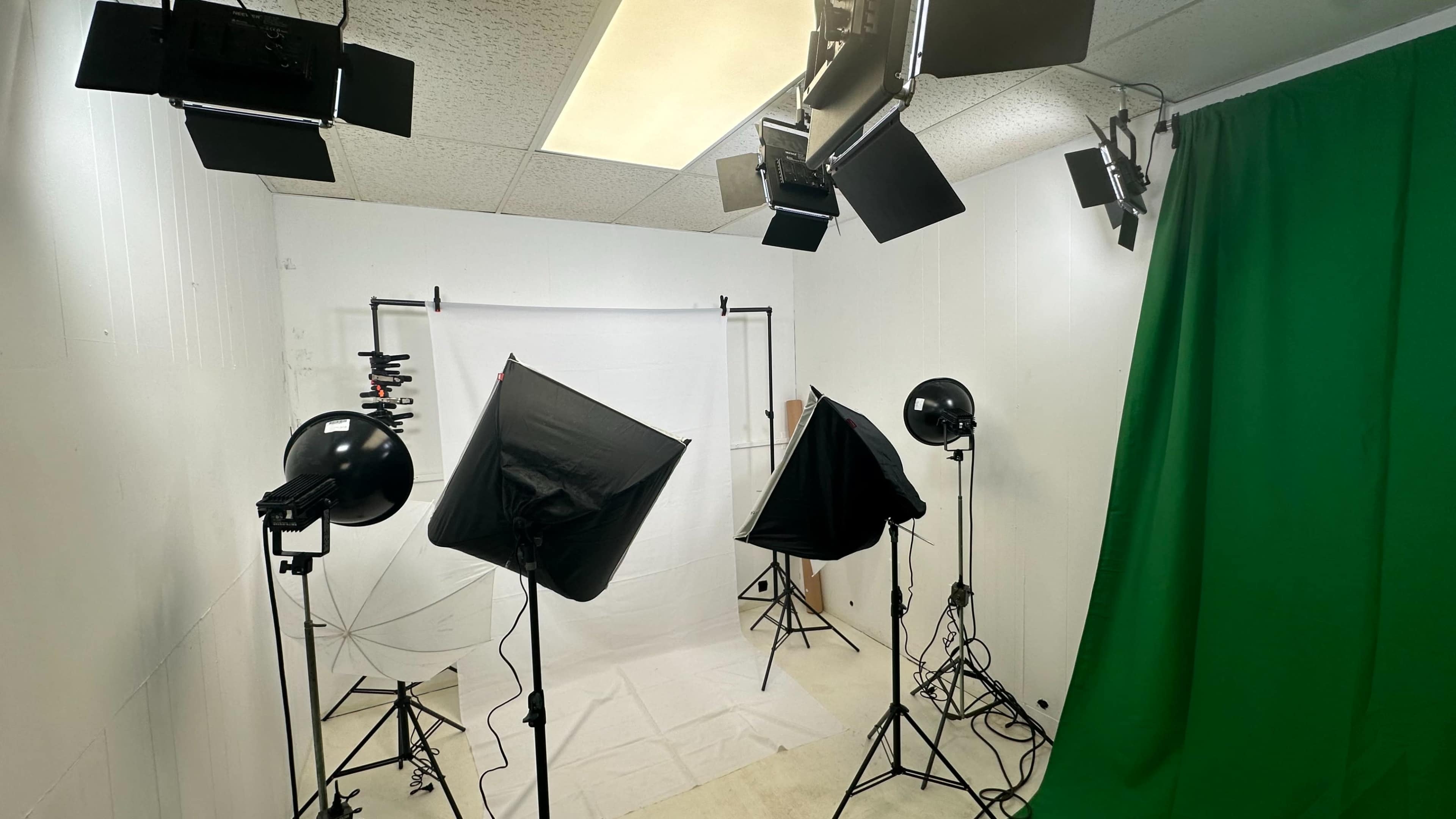 A photography studio equipped with various lighting setups, a white backdrop, and a green screen.