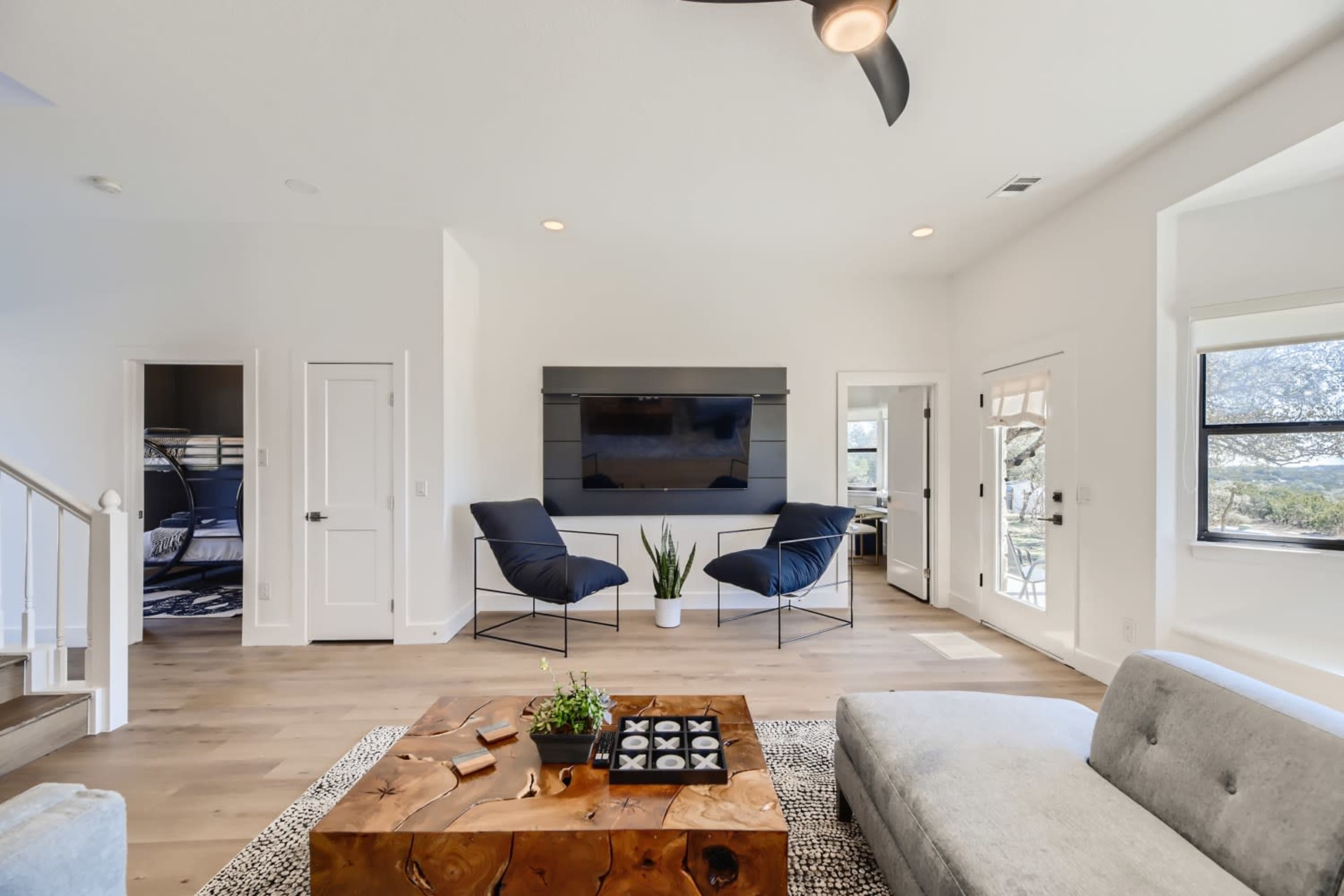 A modern living room with a light-colored curved sofa, a wooden coffee table, and two black chairs facing a wall-mounted television.