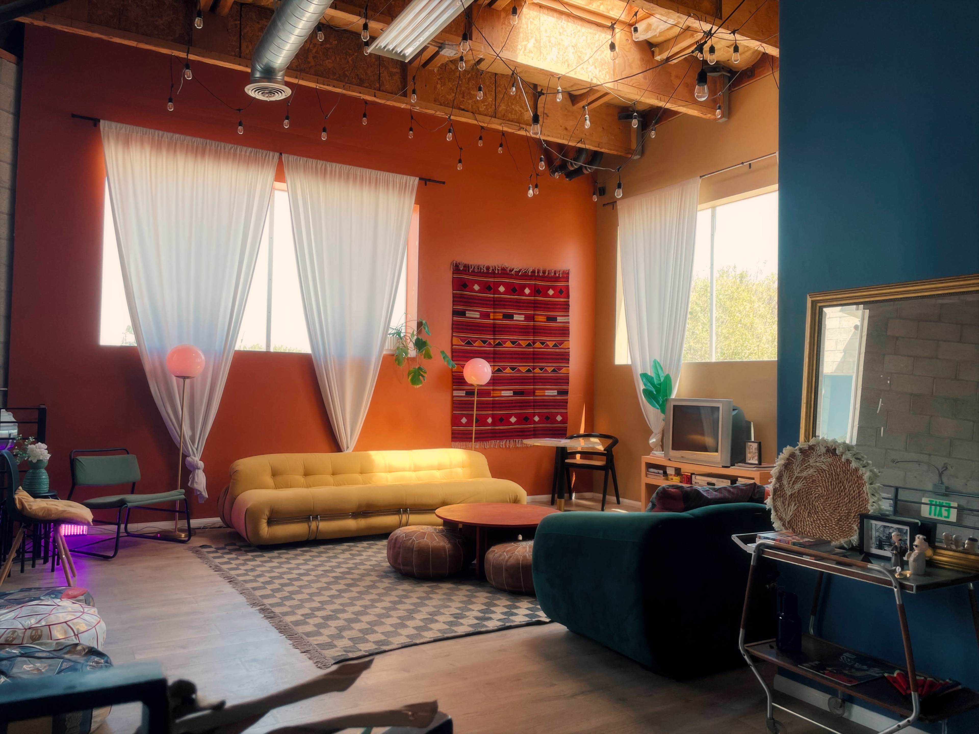 The image features a cozy living space with large windows, colorful walls, and various seating options, including a yellow sofa and dark green armchair.