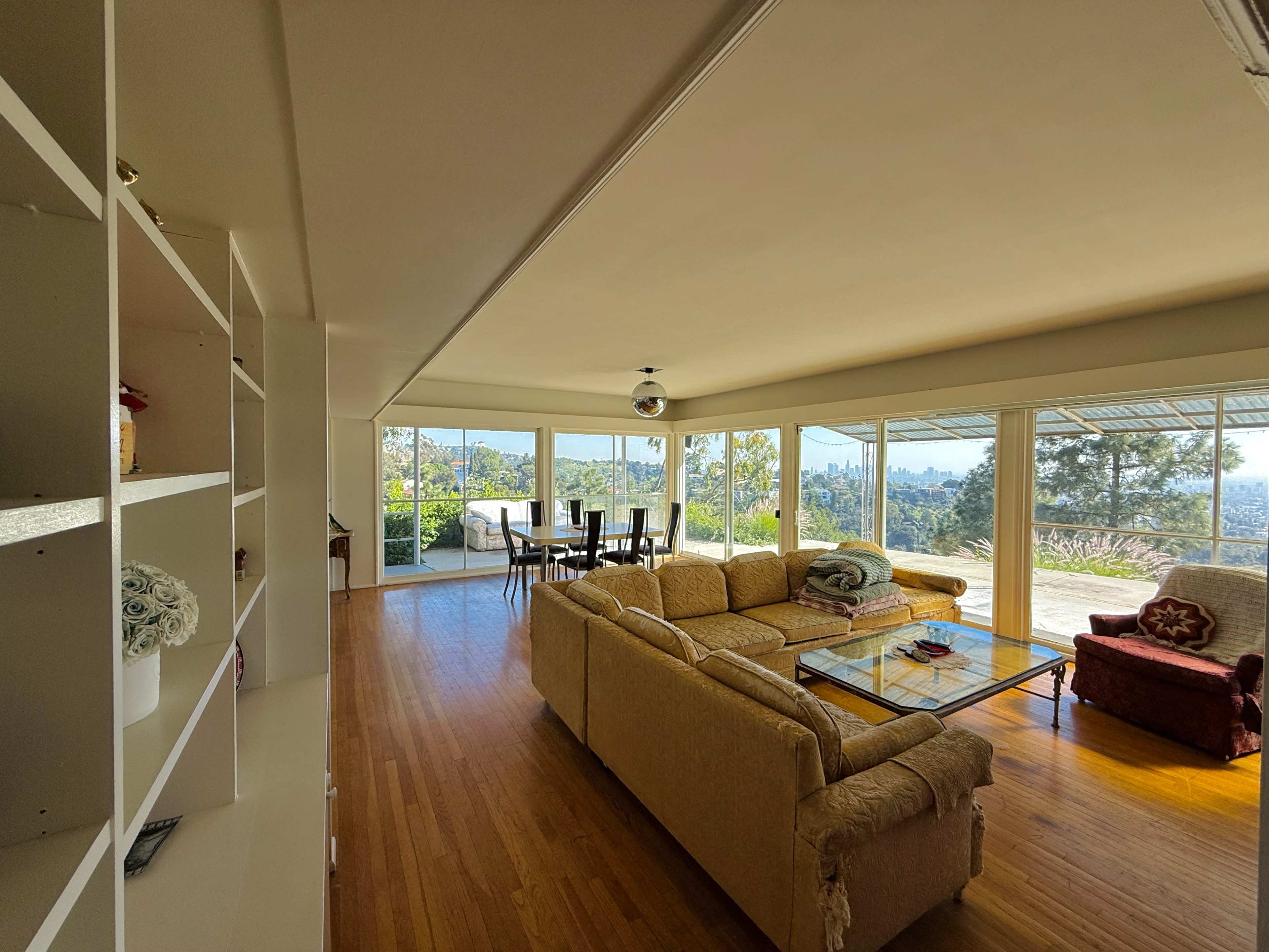 The image shows a spacious living area with a large sofa, a glass coffee table, and a dining table visible through large windows overlooking a view.
