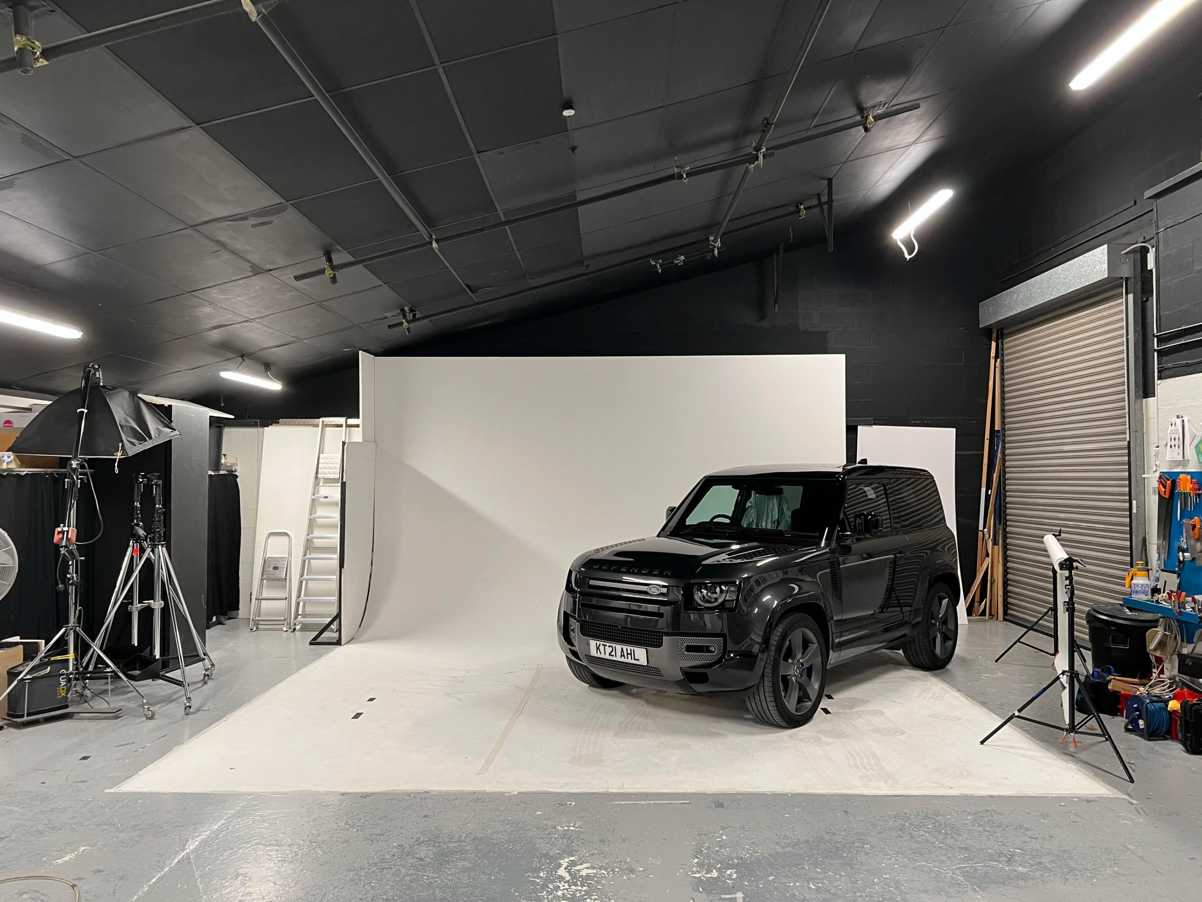 A black SUV is parked in a photography studio with a white backdrop and various equipment set around the space.