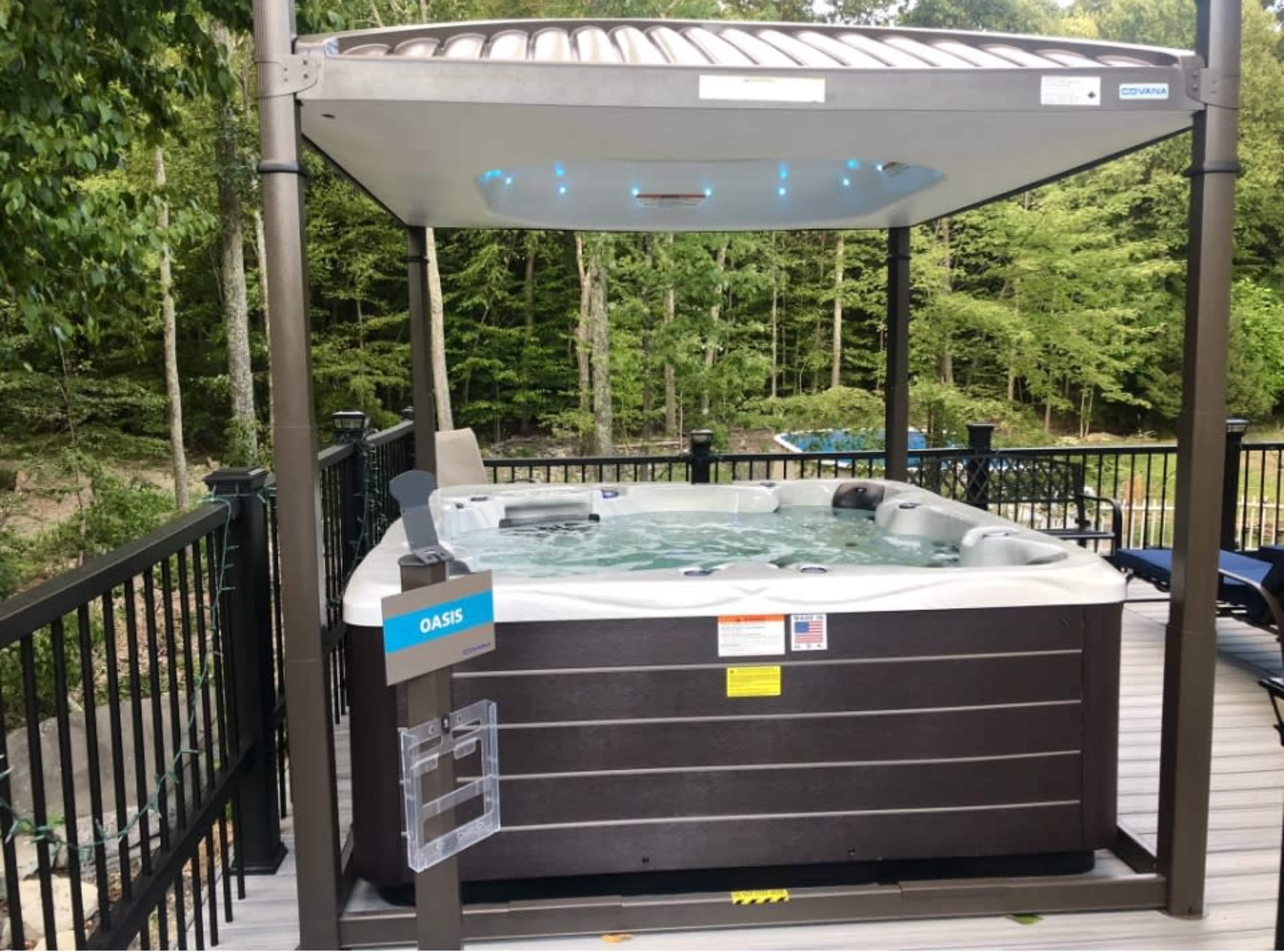 A hot tub sits beneath a canopy in a forested outdoor area on a wooden deck.