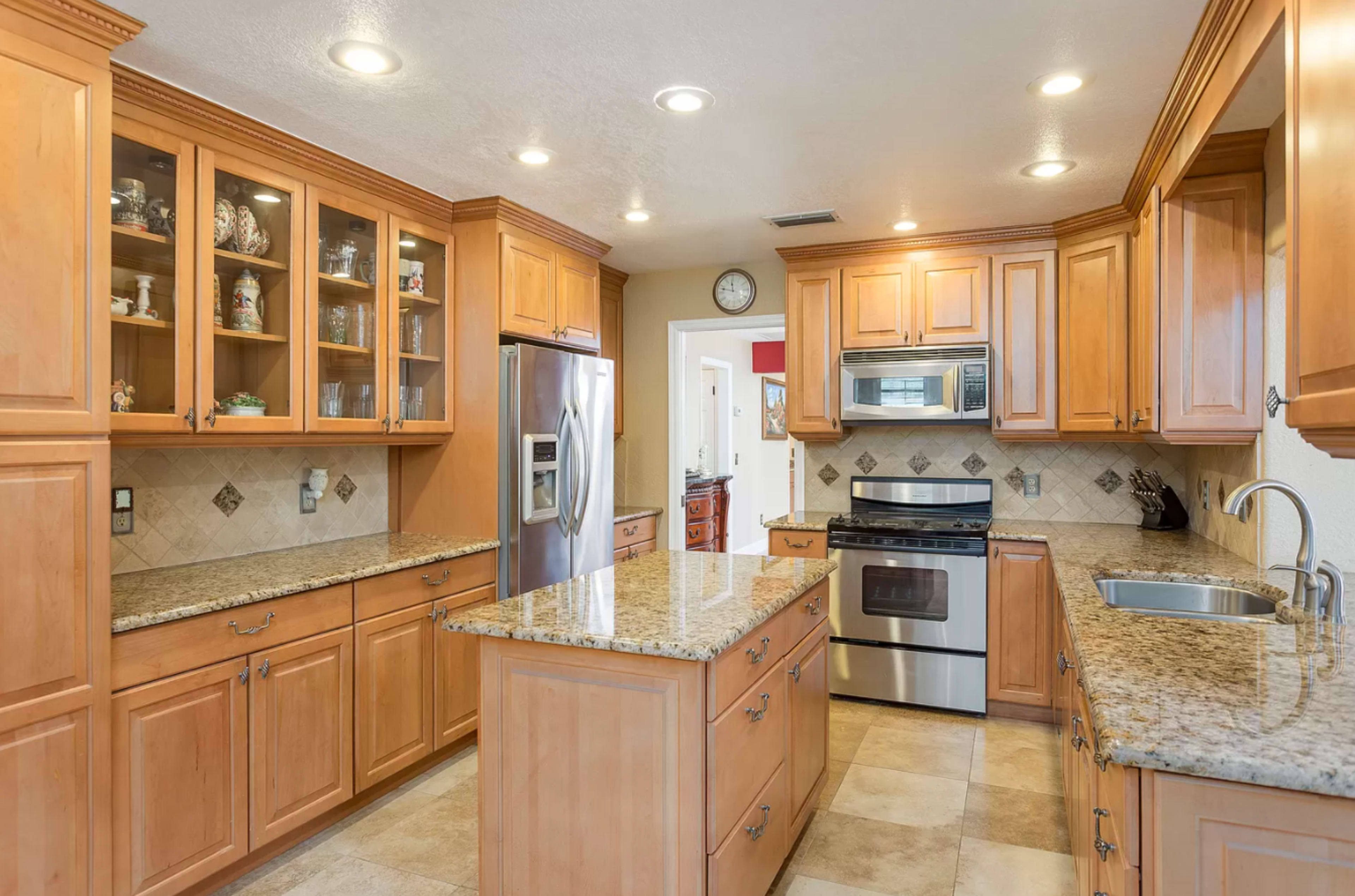 A modern kitchen features wooden cabinets, stainless steel appliances, and a large central island with a granite countertop.