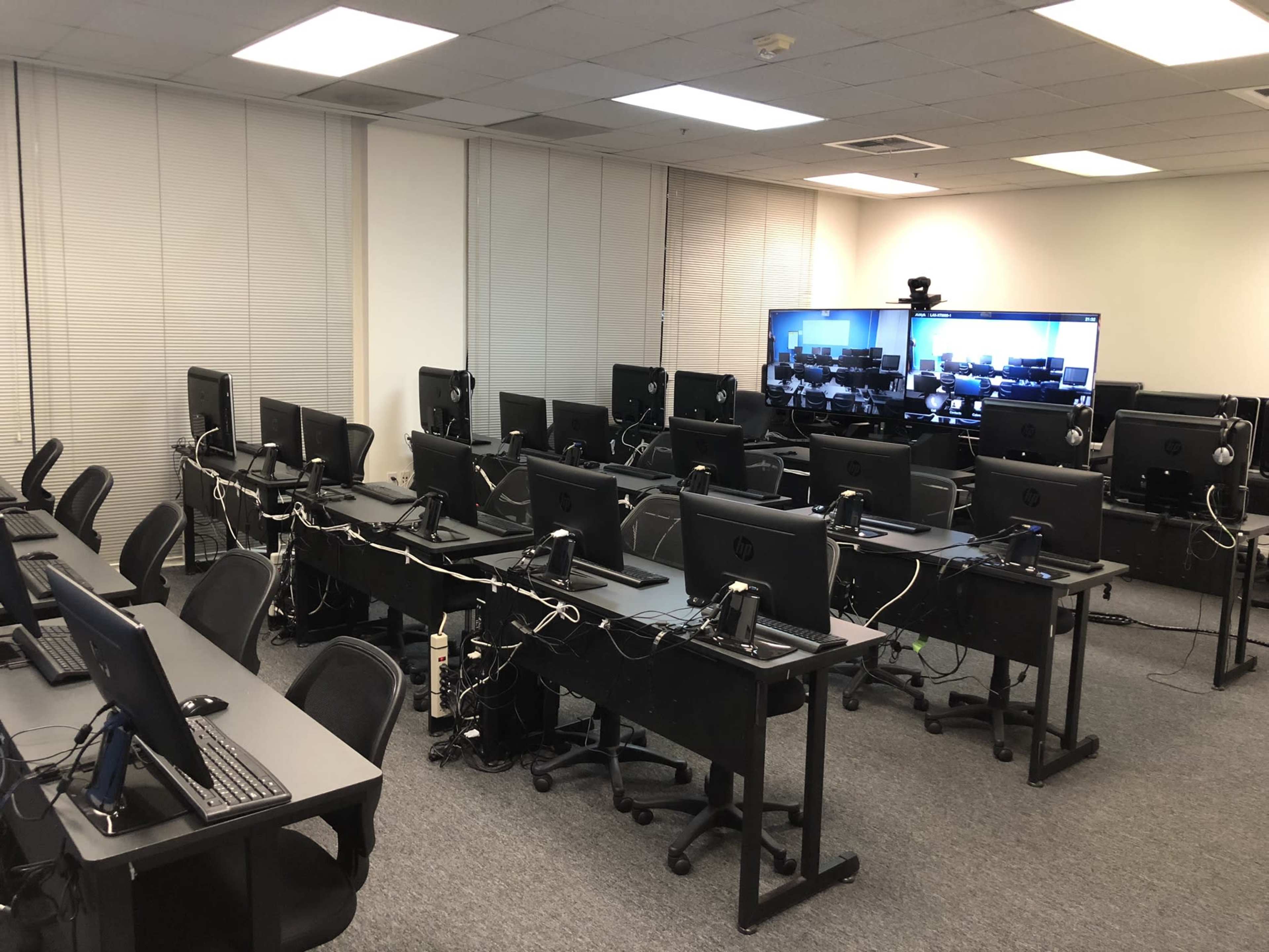 A computer lab with multiple workstations, each equipped with monitors, keyboards, and headsets, arranged in a systematic layout.