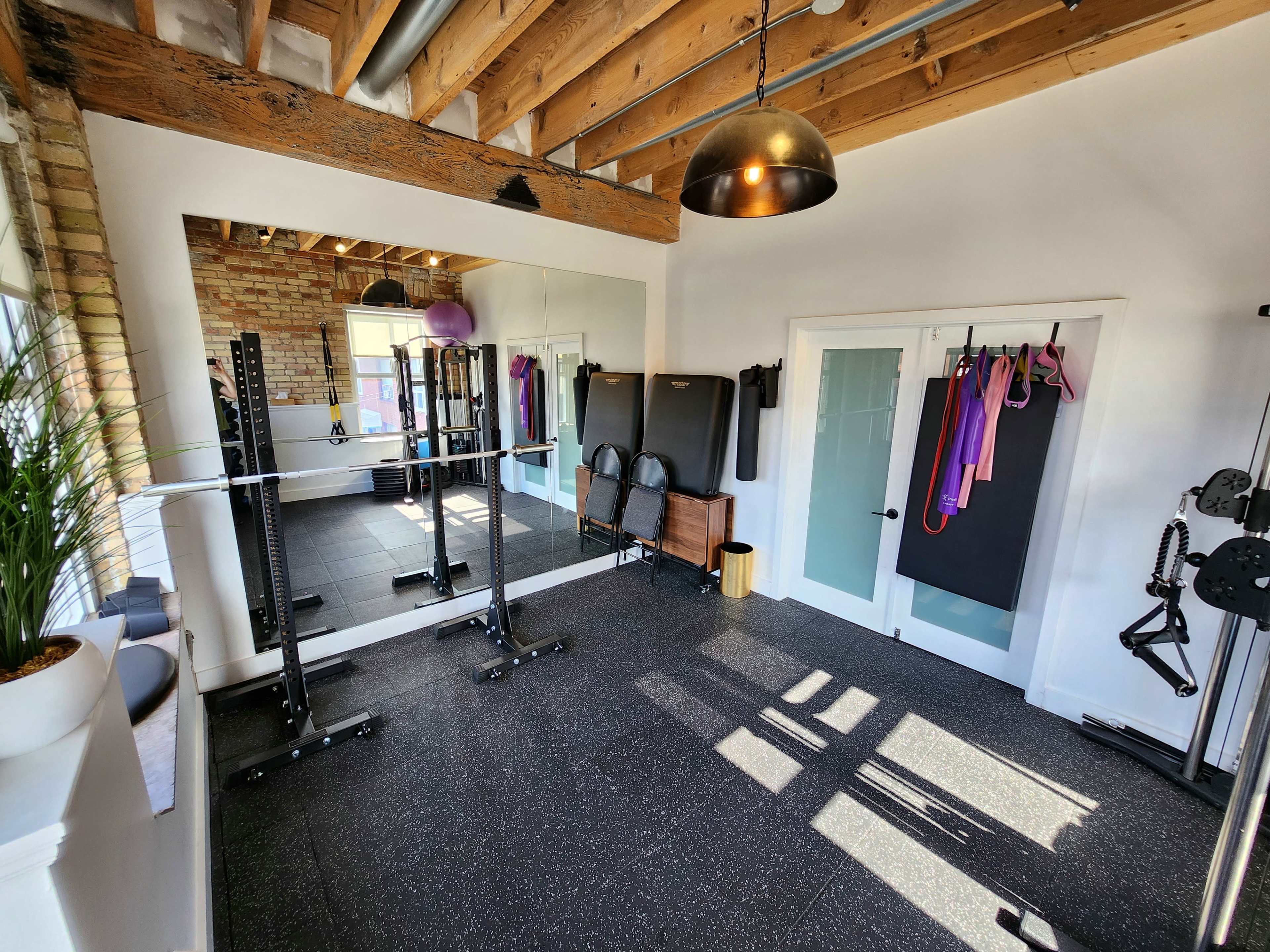 A well-lit home gym with a mirrored wall, exercise equipment, and a wooden beam ceiling.