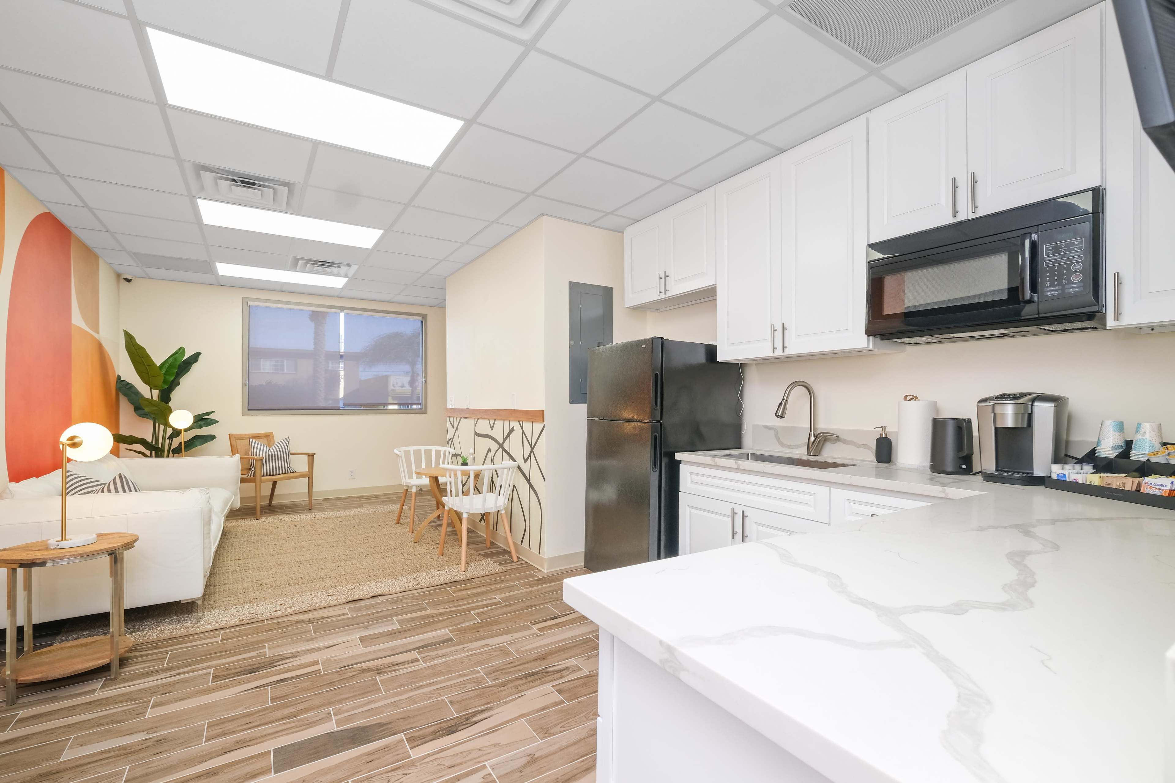 A modern kitchen and living area with white cabinets, a black refrigerator, and a cozy seating space featuring a couch and chairs.