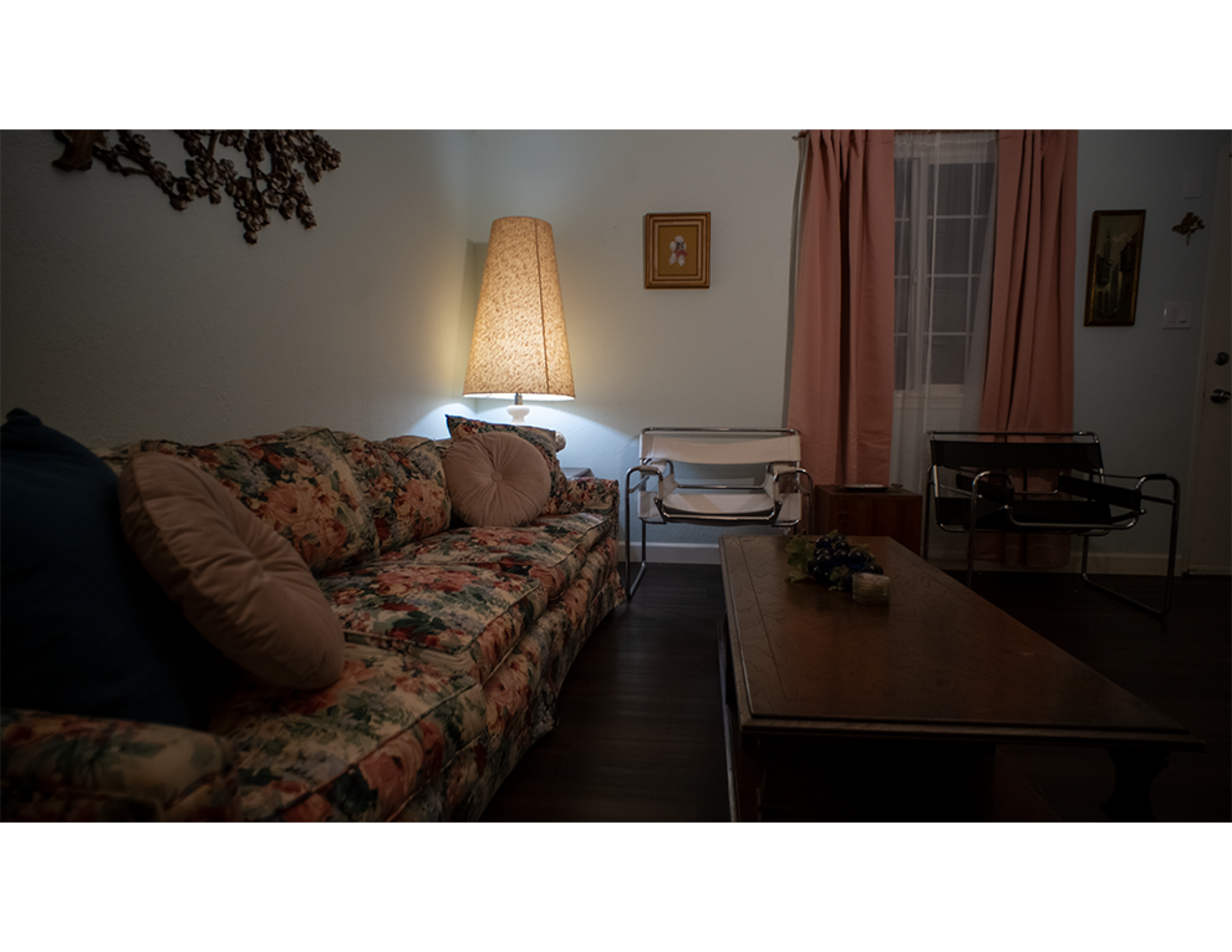 A cozy living room with a floral couch, a wooden coffee table, and a standing lamp casting soft light.