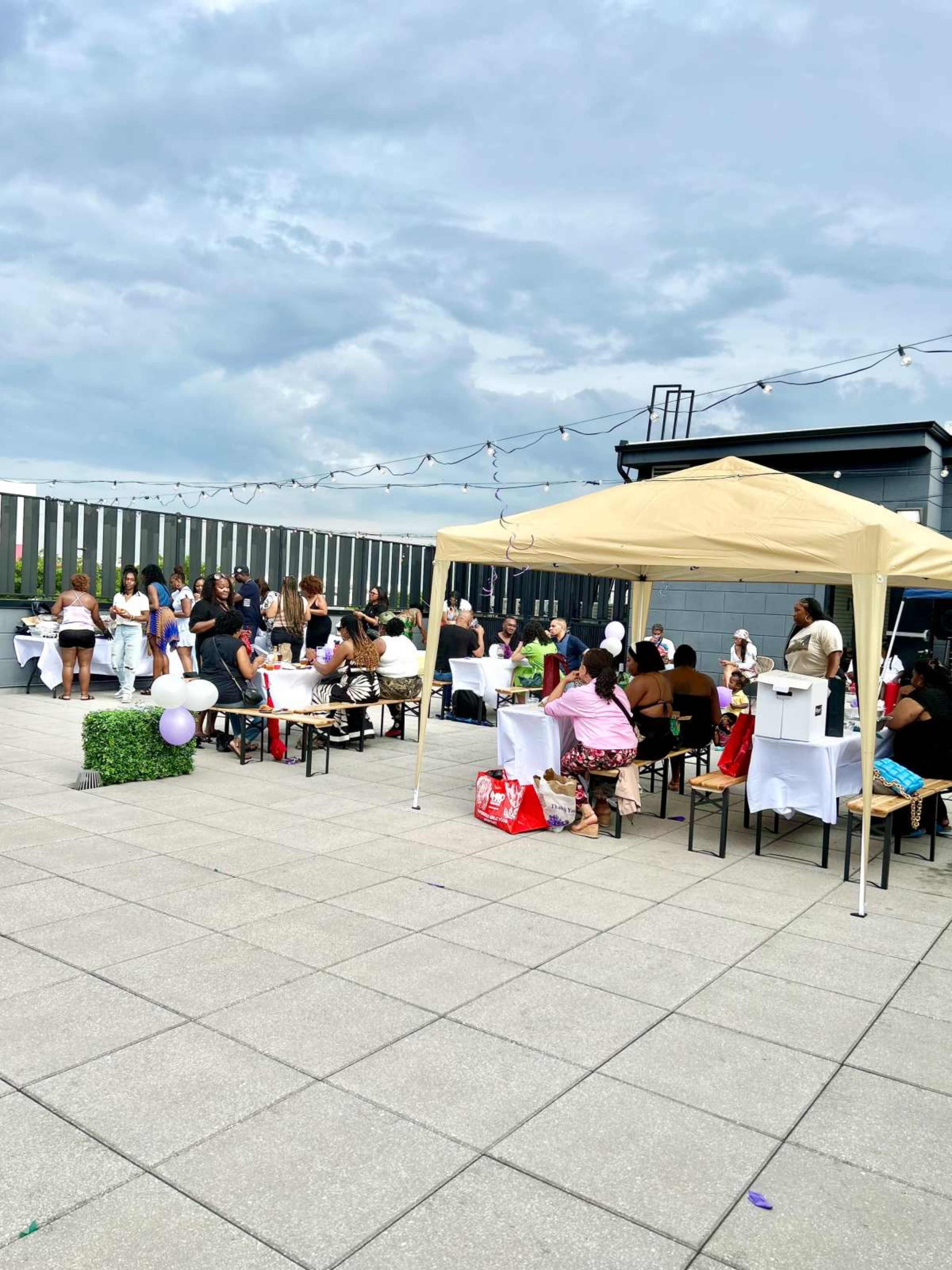 A group of people socializes under a canopy at a rooftop event, surrounded by tables and decorative elements.