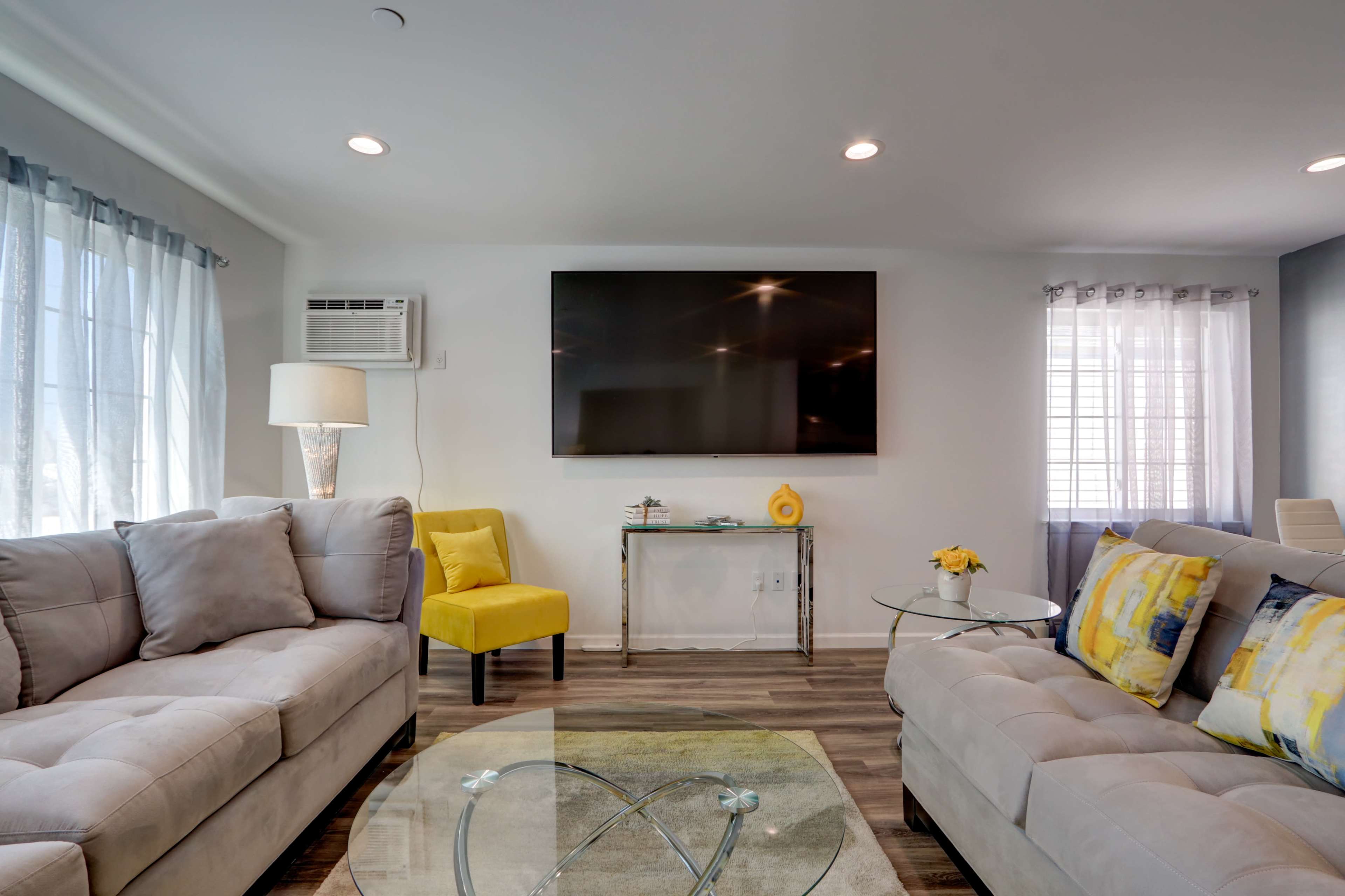 The living room features a gray sectional sofa, a yellow accent chair, a glass coffee table, and a wall-mounted television.