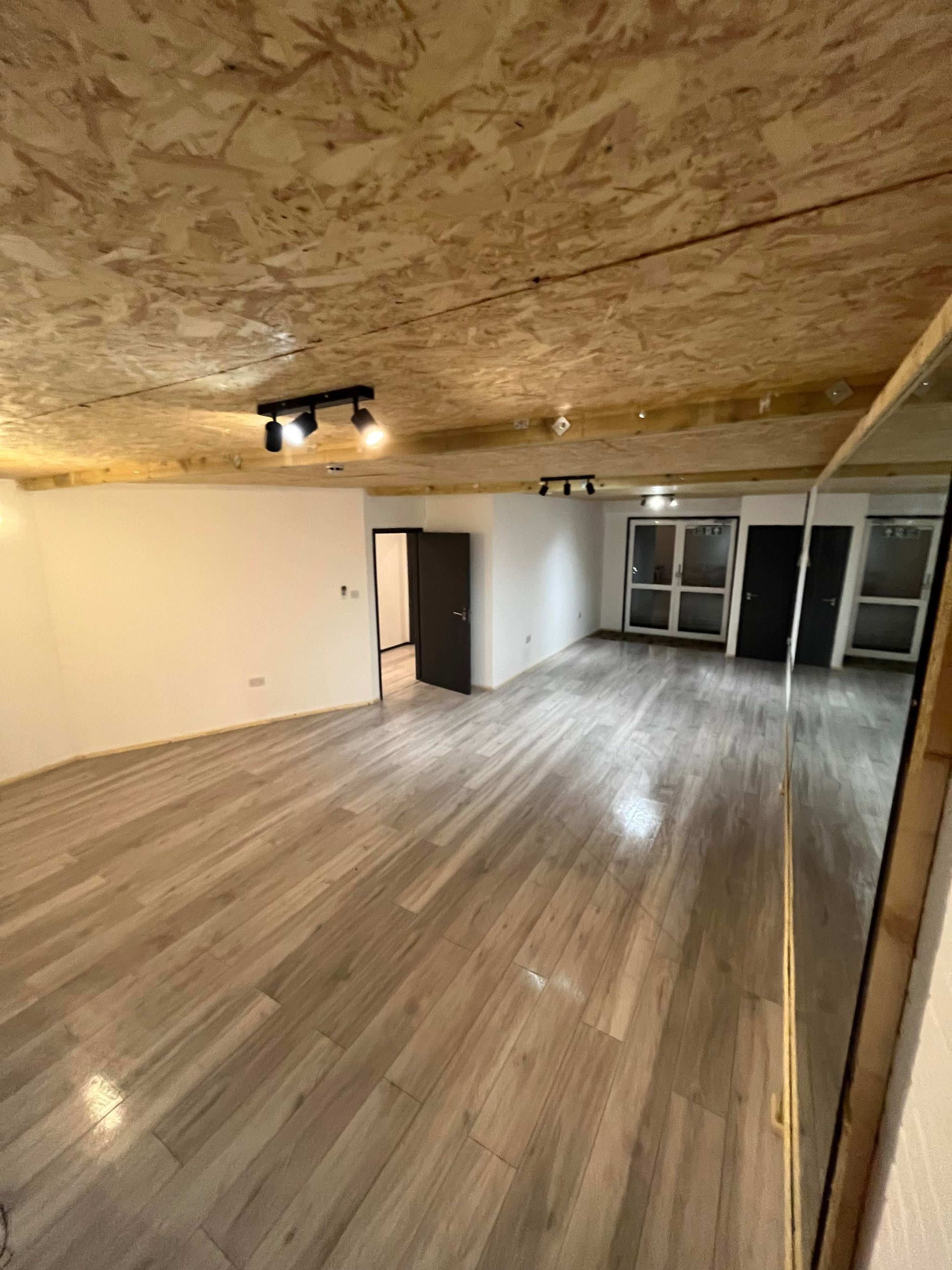 An empty room features a wood-paneled ceiling, wooden flooring, and multiple doors leading to other spaces.
