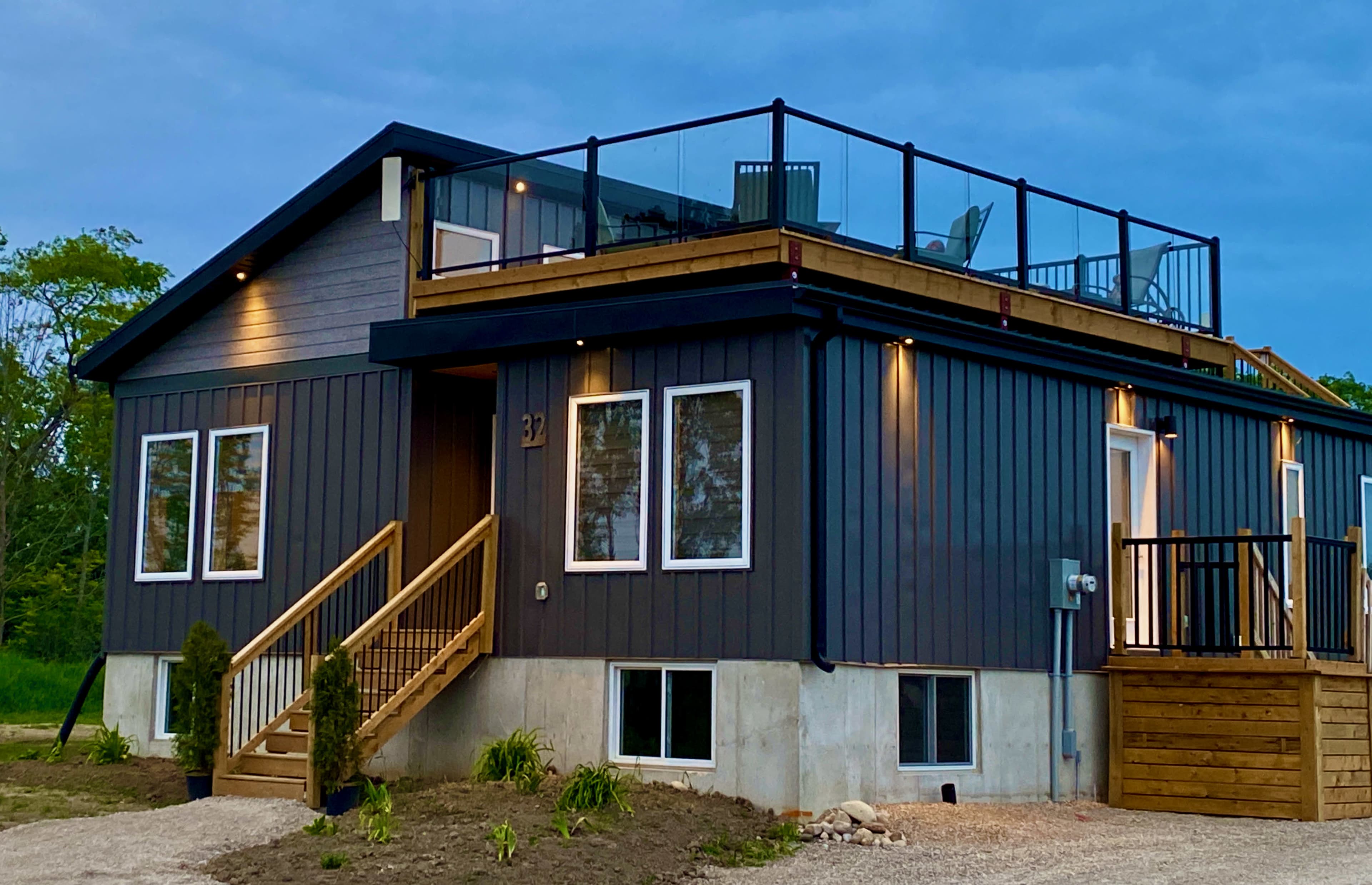 A modern two-story house with a wooden deck and railing, a stone pathway, and large windows, set against a cloudy sky.