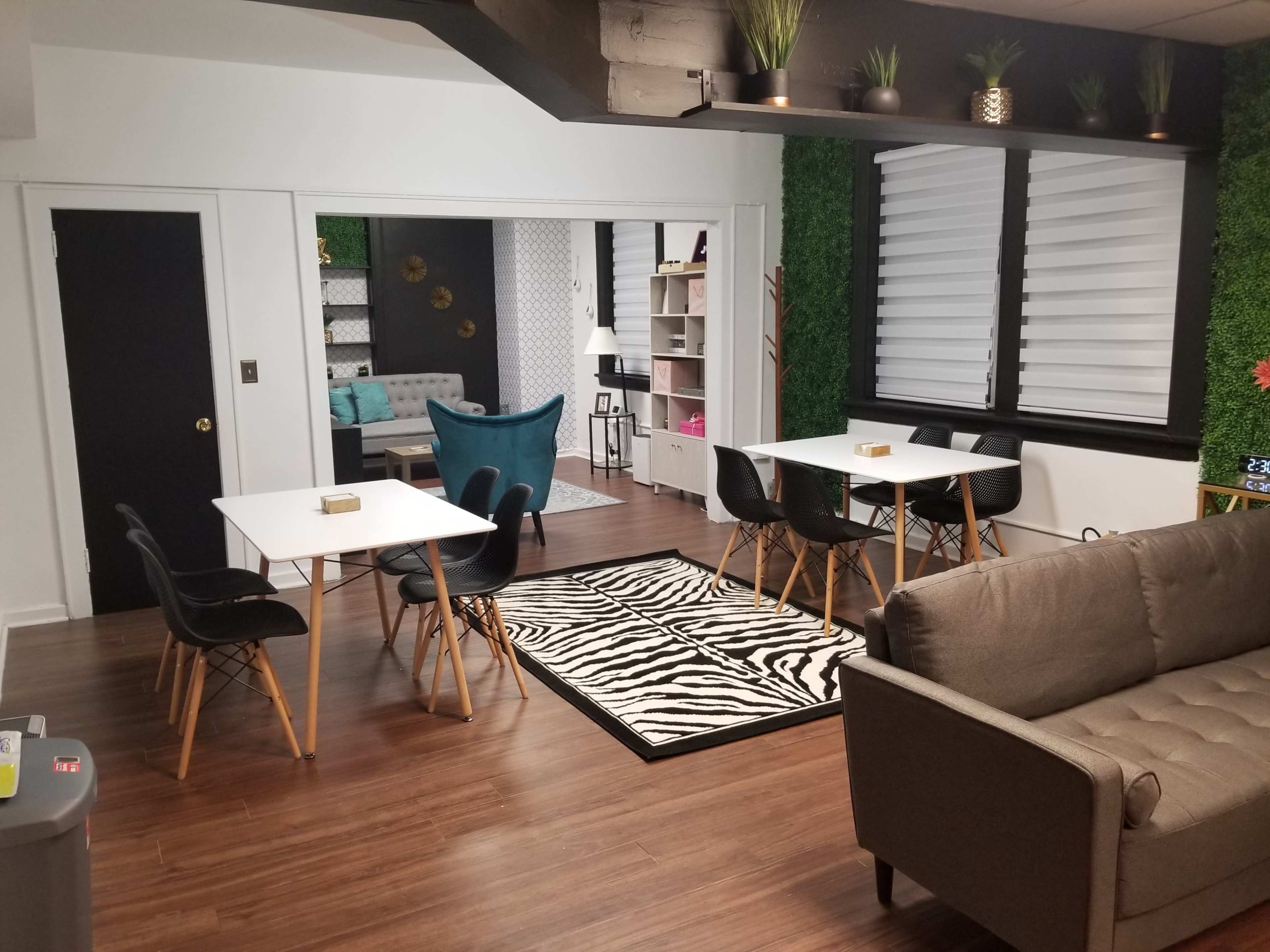 A modern multi-functional room featuring several tables and chairs, a couch, and a partitioned area with plants and decorative elements.