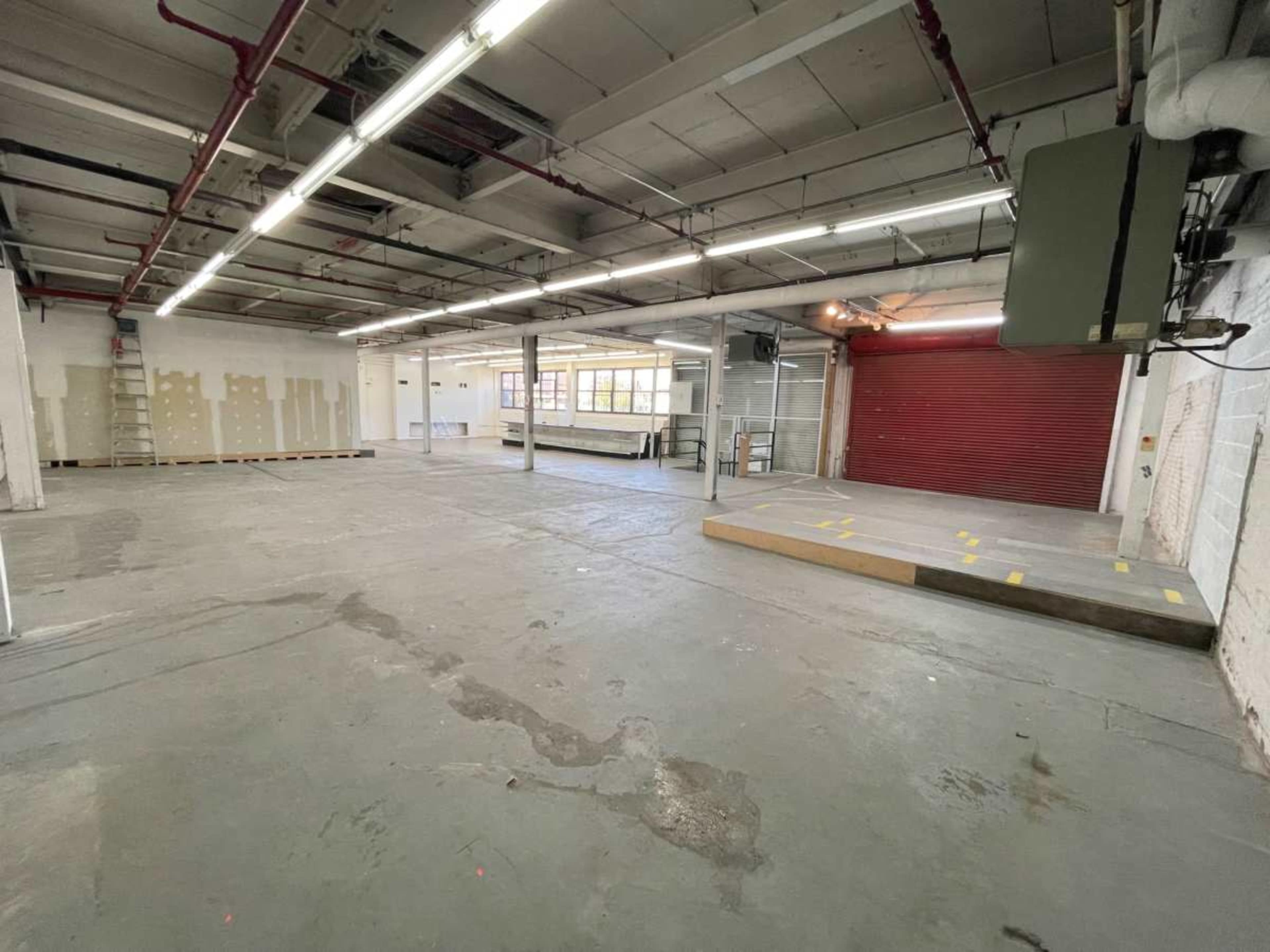 The image shows an empty industrial space with a concrete floor, red roll-up door, and fluorescent lighting.
