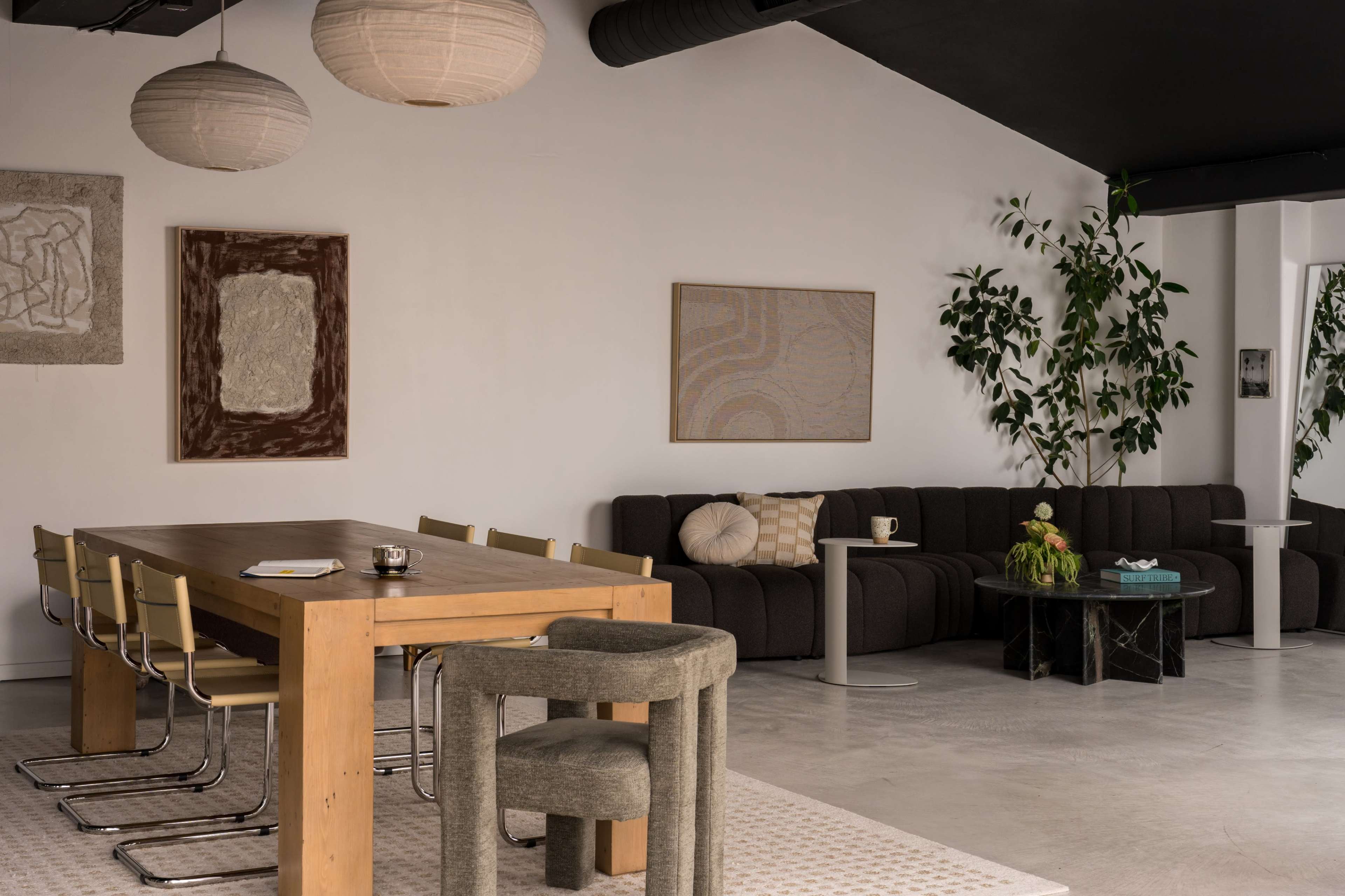 The image features a modern living space with a wooden dining table, metal chairs, a dark sofa, and decorative wall art, illuminated by pendant lights.