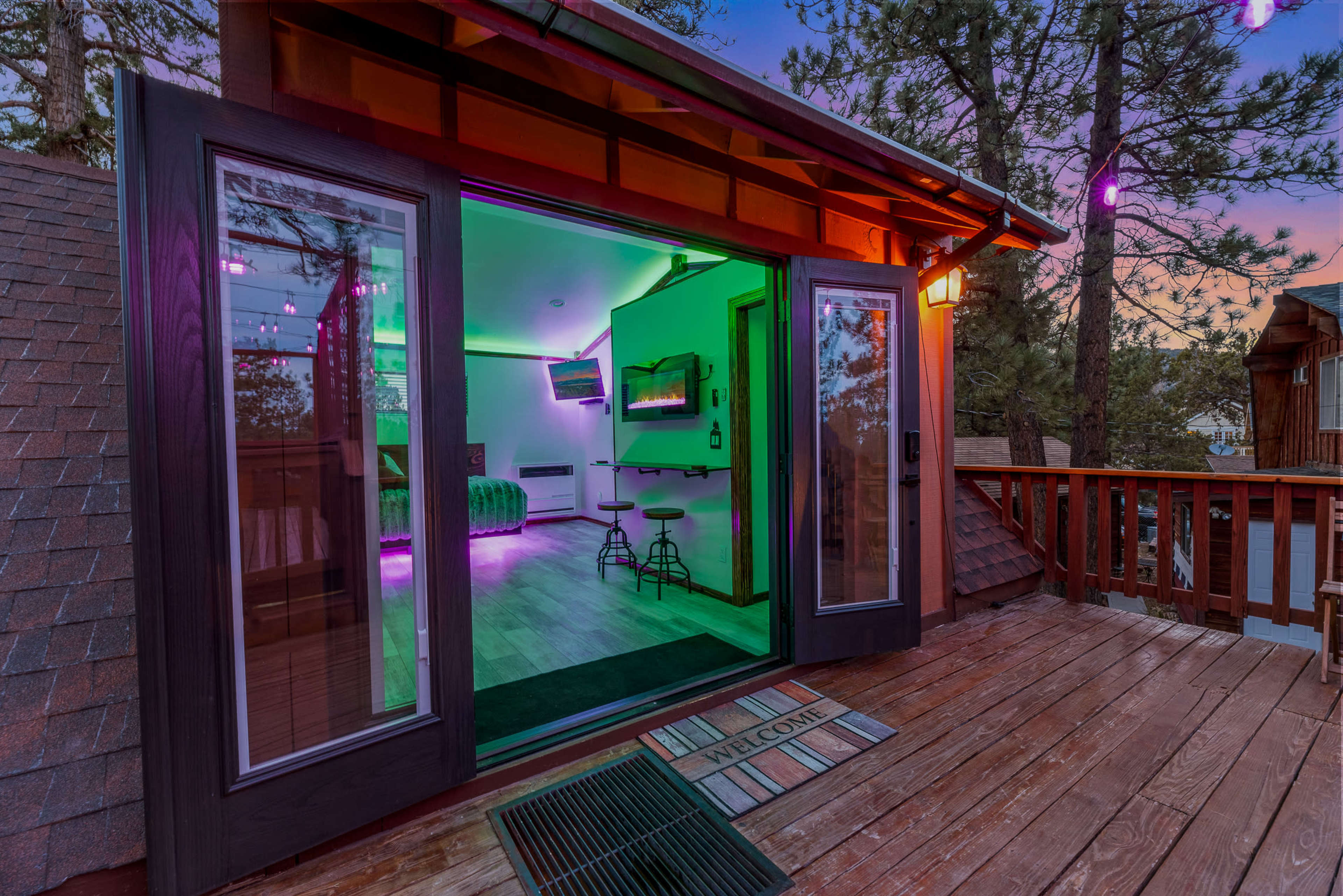A doorway leads to a brightly lit room with modern decor, overlooking a wooden deck surrounded by trees.