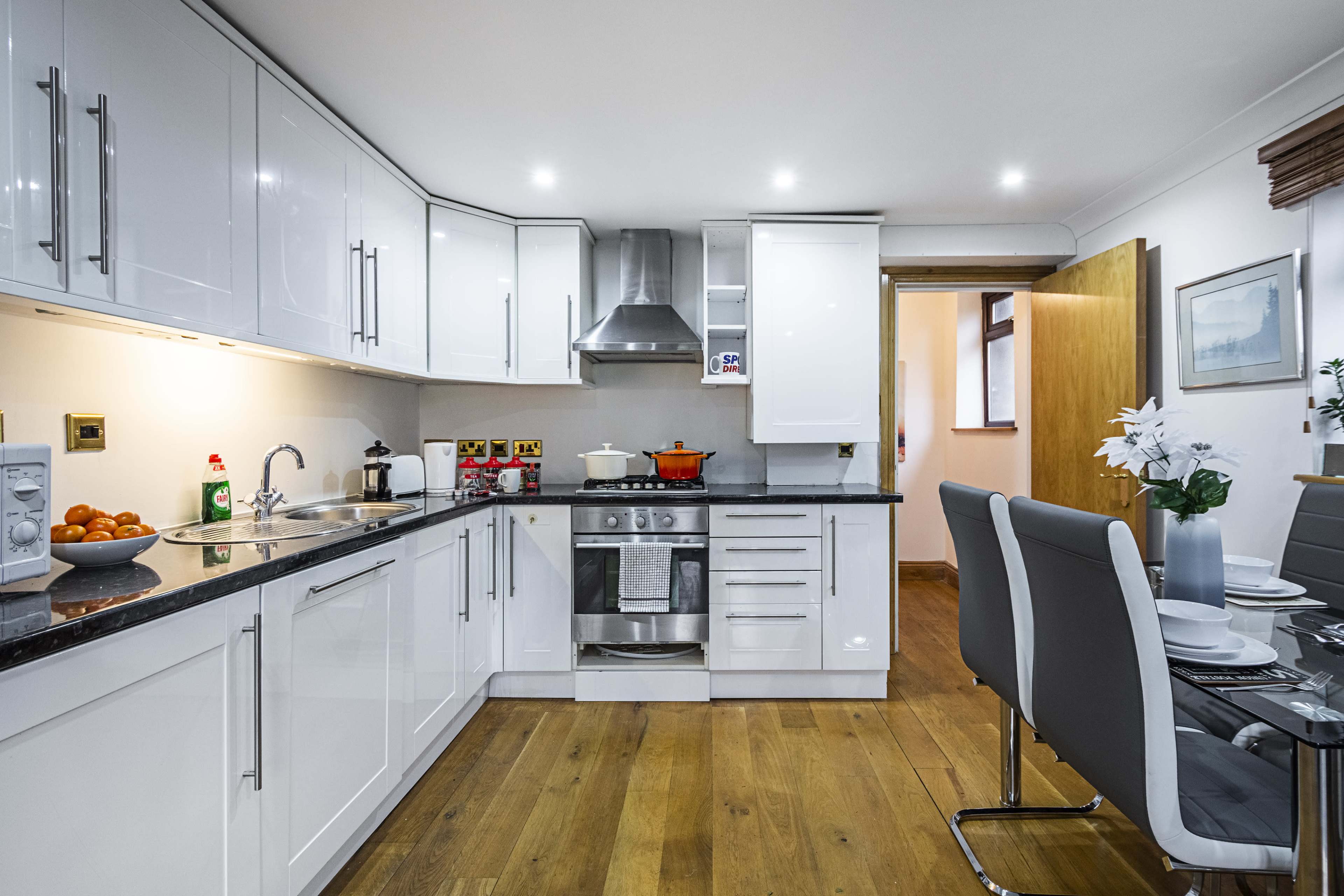 The kitchen features modern white cabinetry, a stainless steel stove and hood, and a dining area with a glass table and chairs.