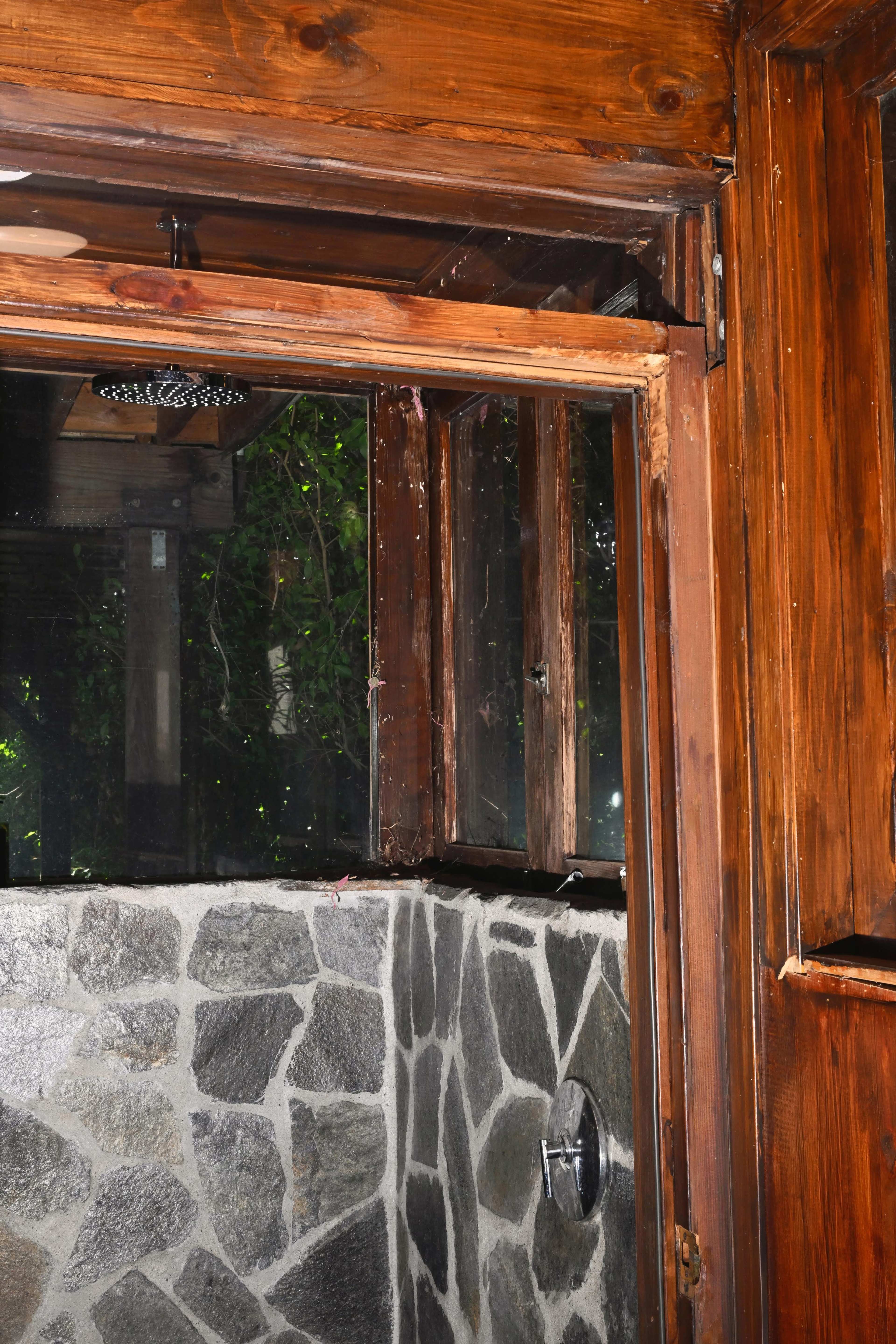 The image shows a wooden-framed shower with stone walls and an open glass enclosure.