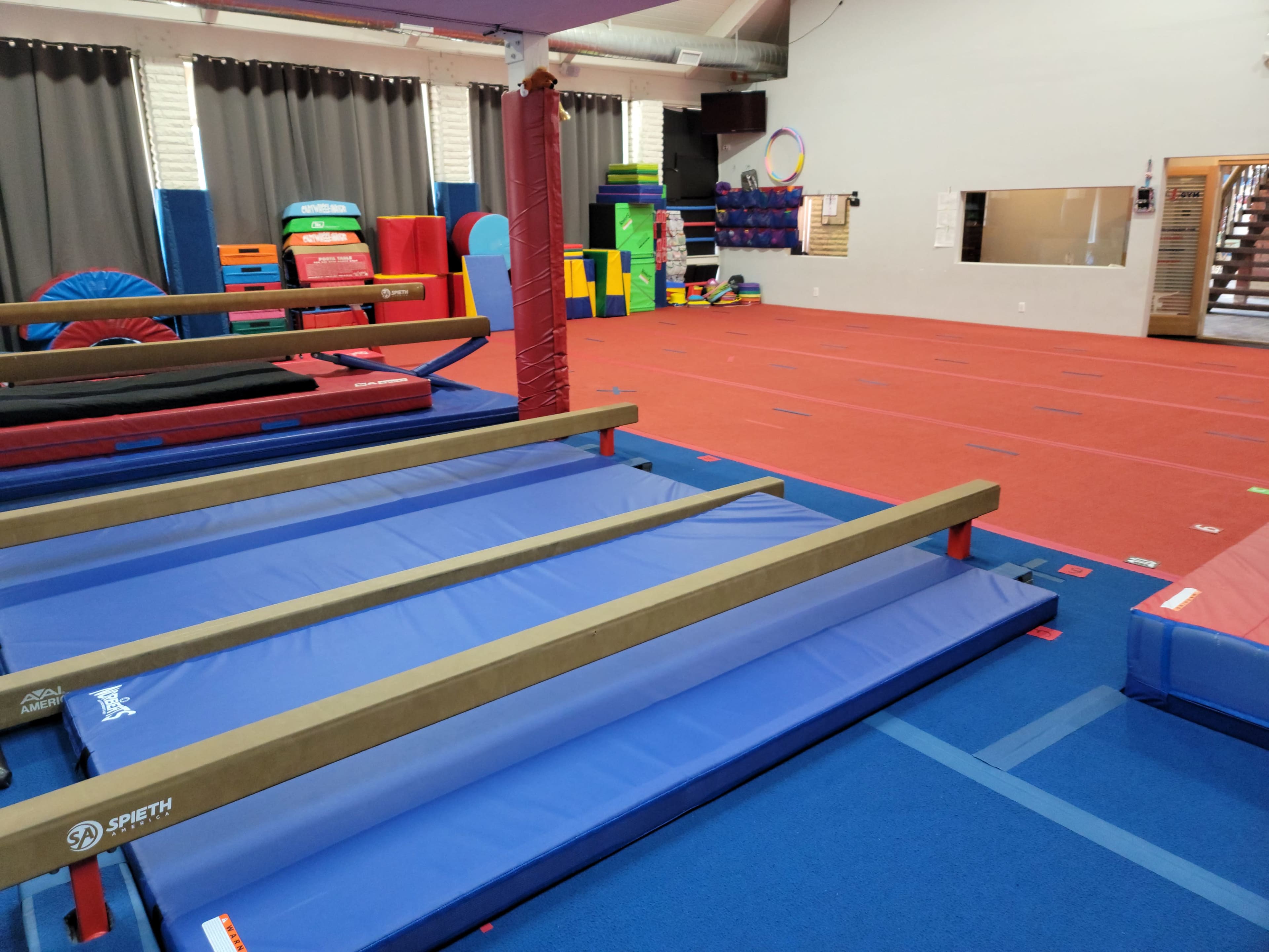 A gymnasium with blue mats, balance beams, and various brightly colored equipment arranged in an open space.