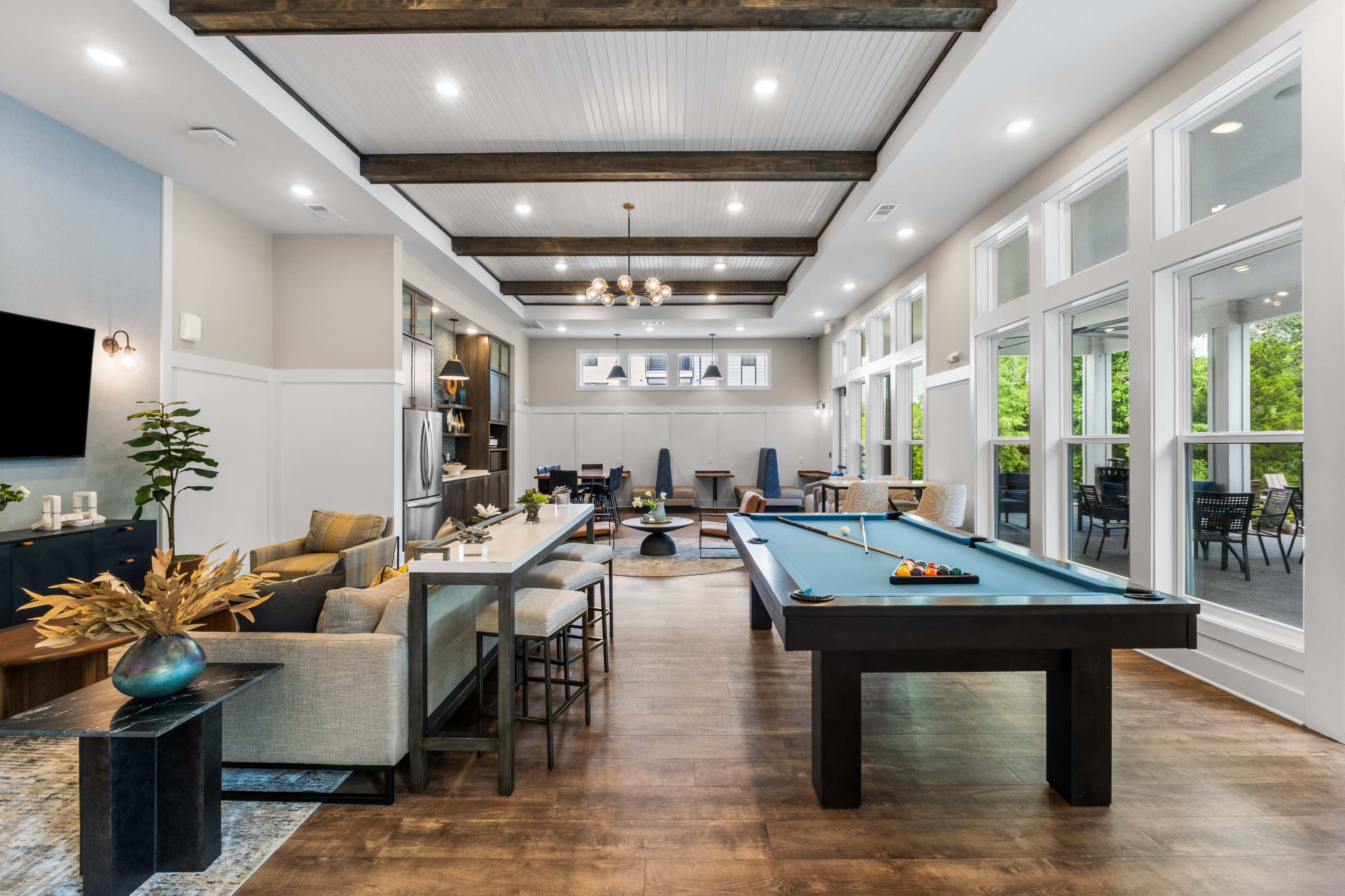 The image showcases a modern game room featuring a billiard table, seating areas, and large windows that allow natural light to fill the space.