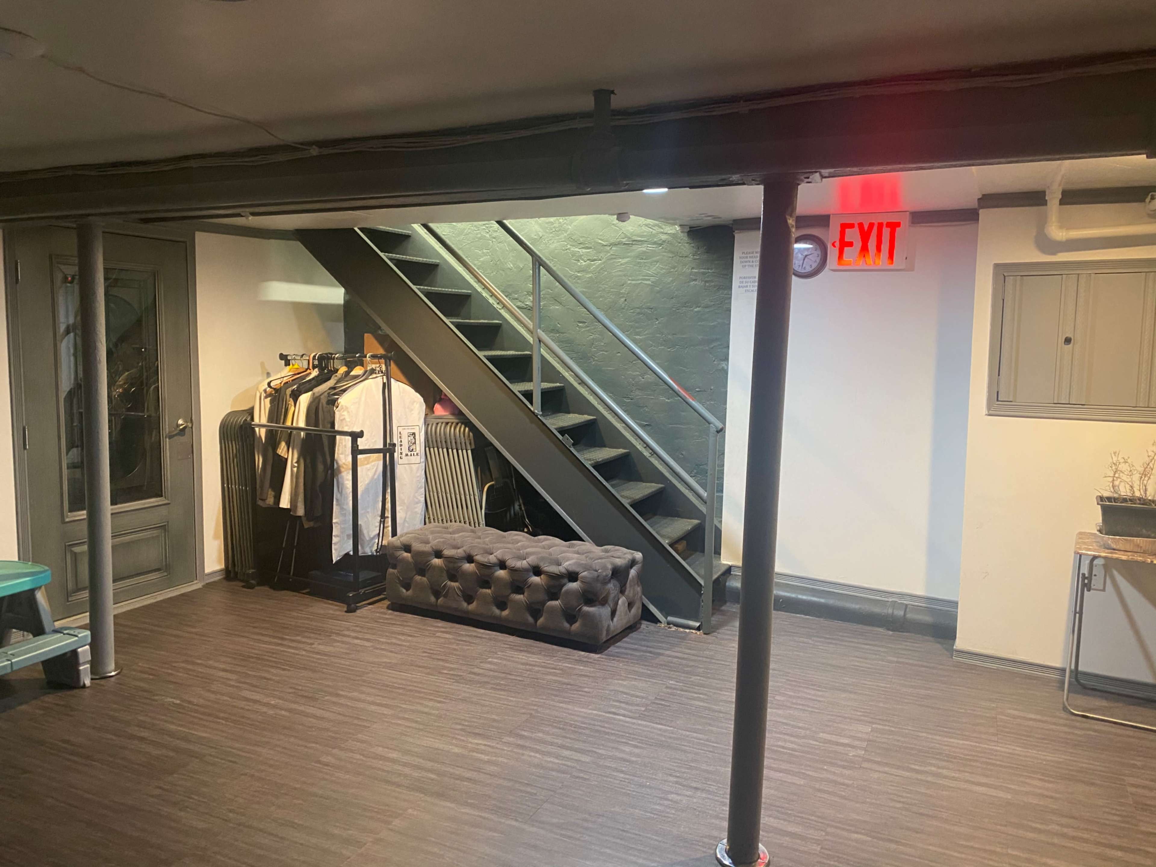 A basement area with a staircase, a tufted bench, and a rack of clothing against the wall.