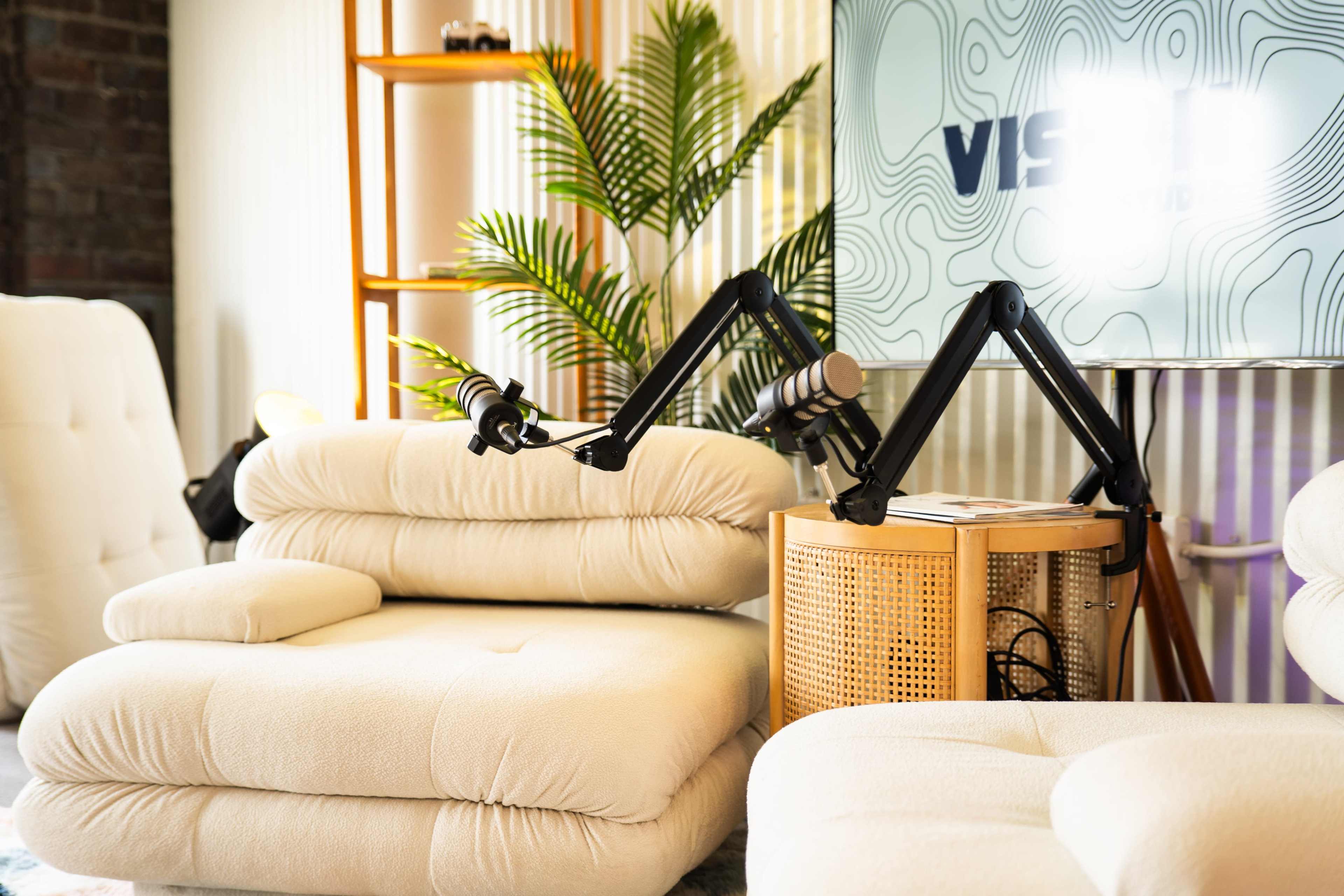 The image shows a cozy seating area with a plush cream-colored couch next to a modern microphone on an adjustable arm and a decorative plant in the background.