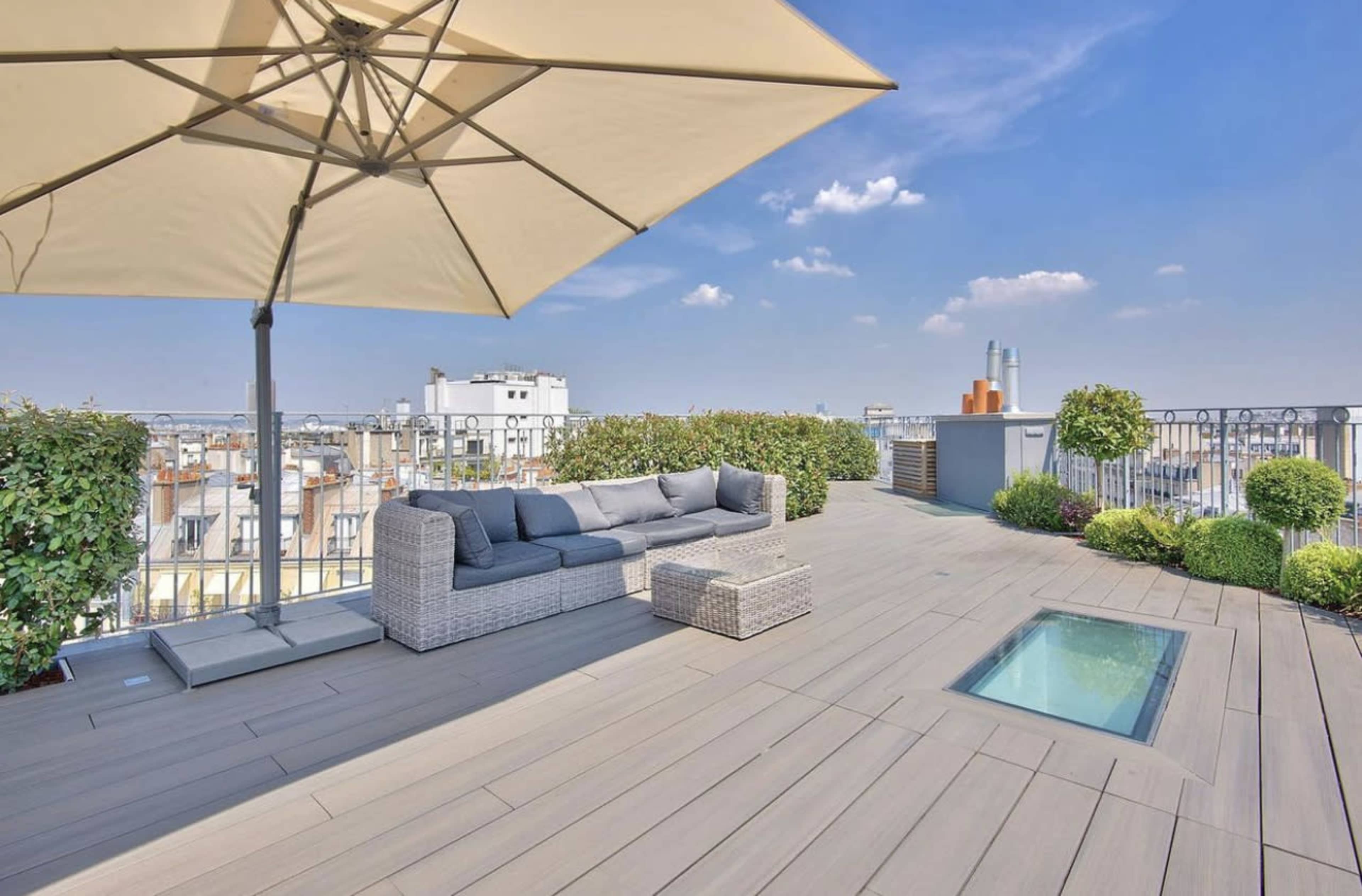 A rooftop terrace features a modern seating area with a large umbrella and a small plunge pool surrounded by greenery.