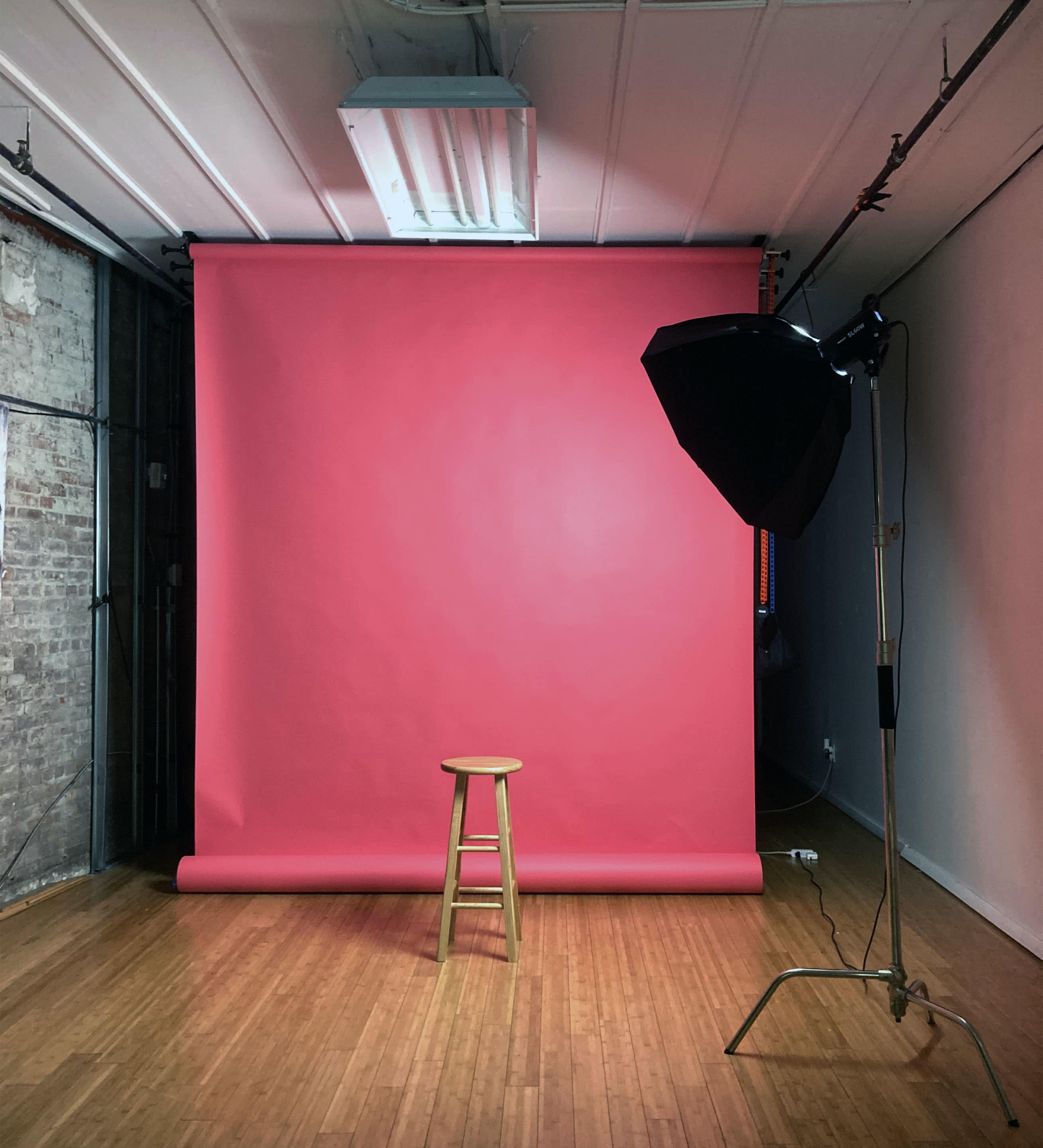 A wooden stool positioned in front of a pink backdrop with a lighting setup in a studio space.
