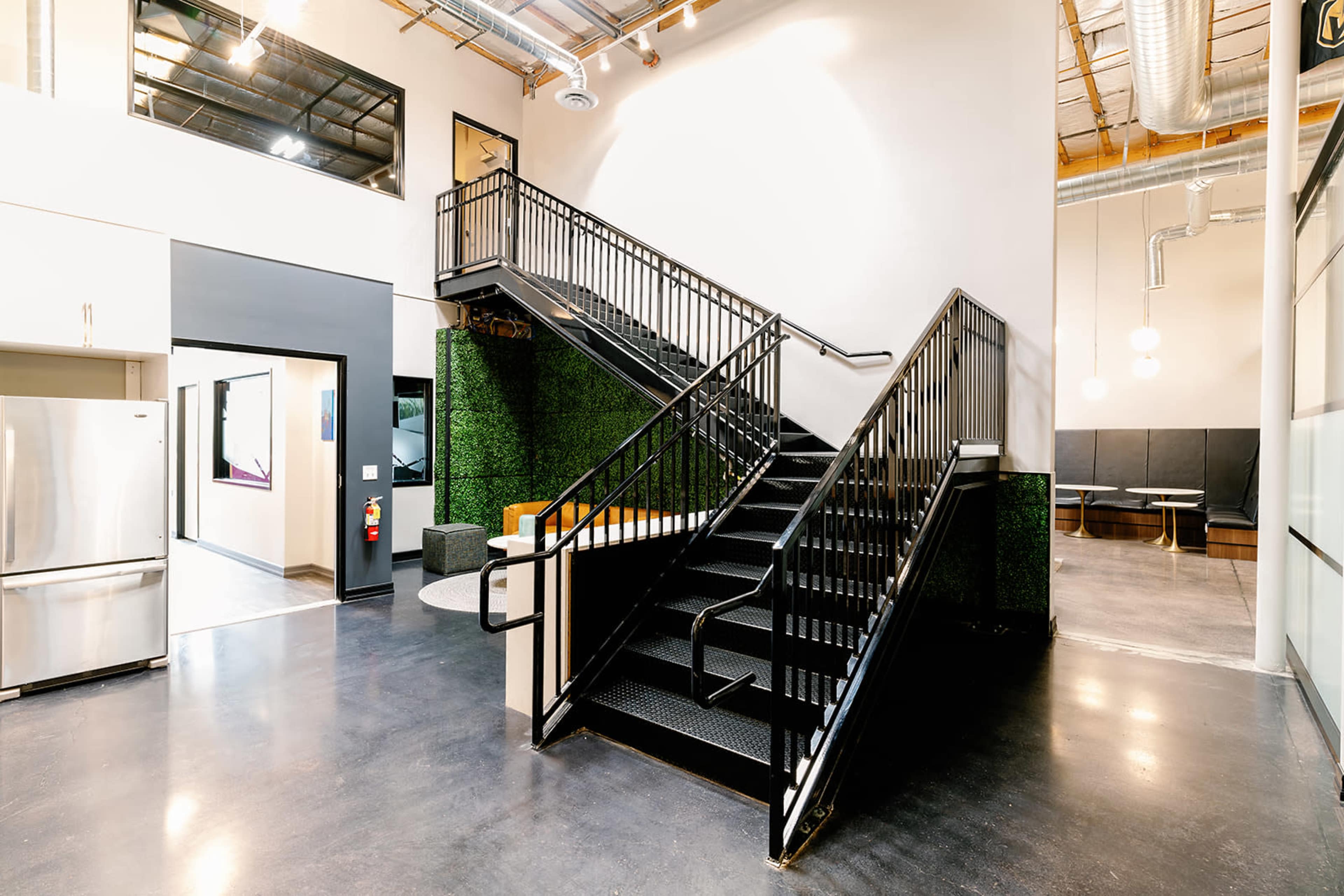 A modern interior space featuring a black metal staircase surrounded by green wall accents and sleek furnishings.