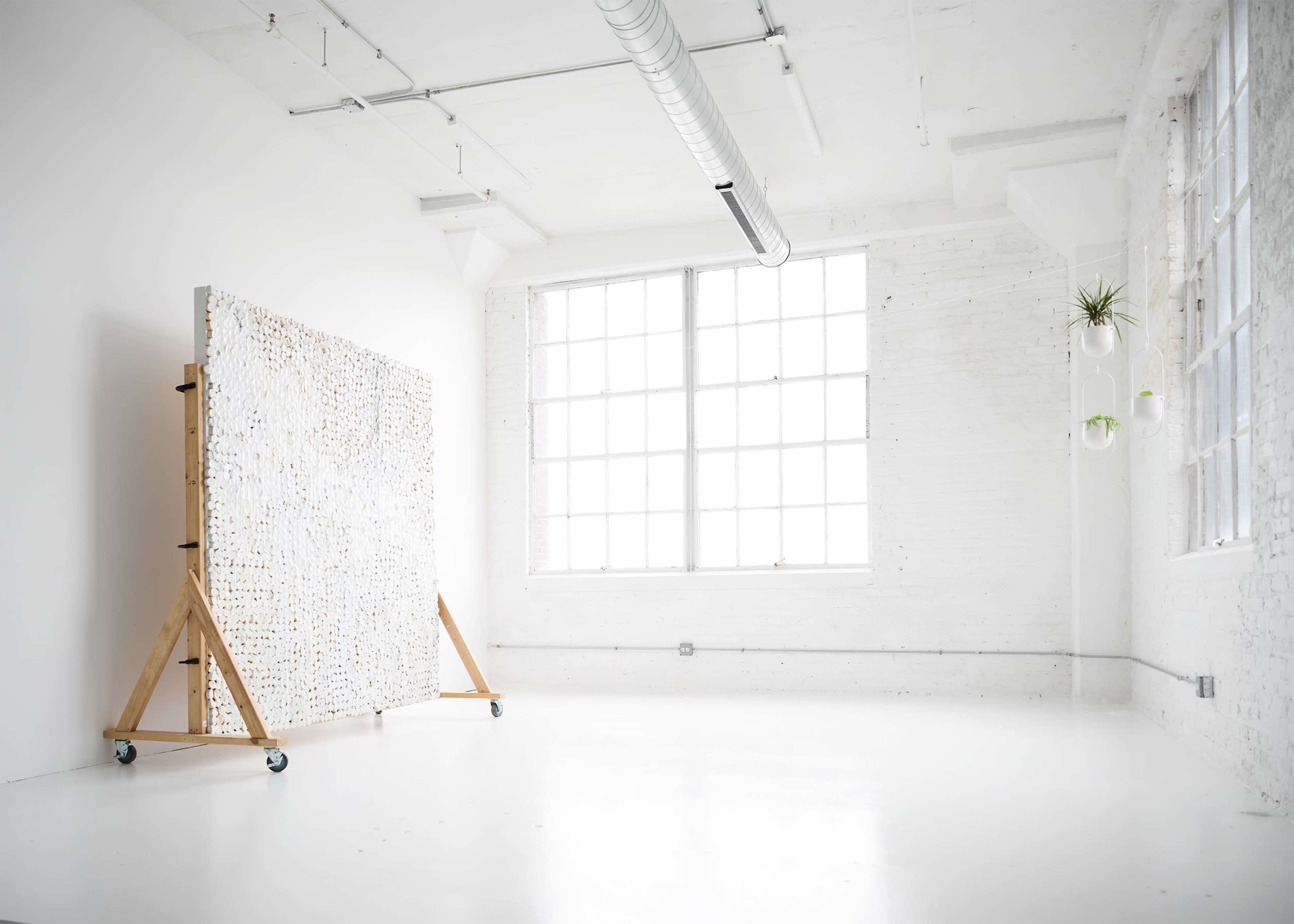 A large abstract art piece is positioned on wheels in a bright, minimalist studio space with large windows.