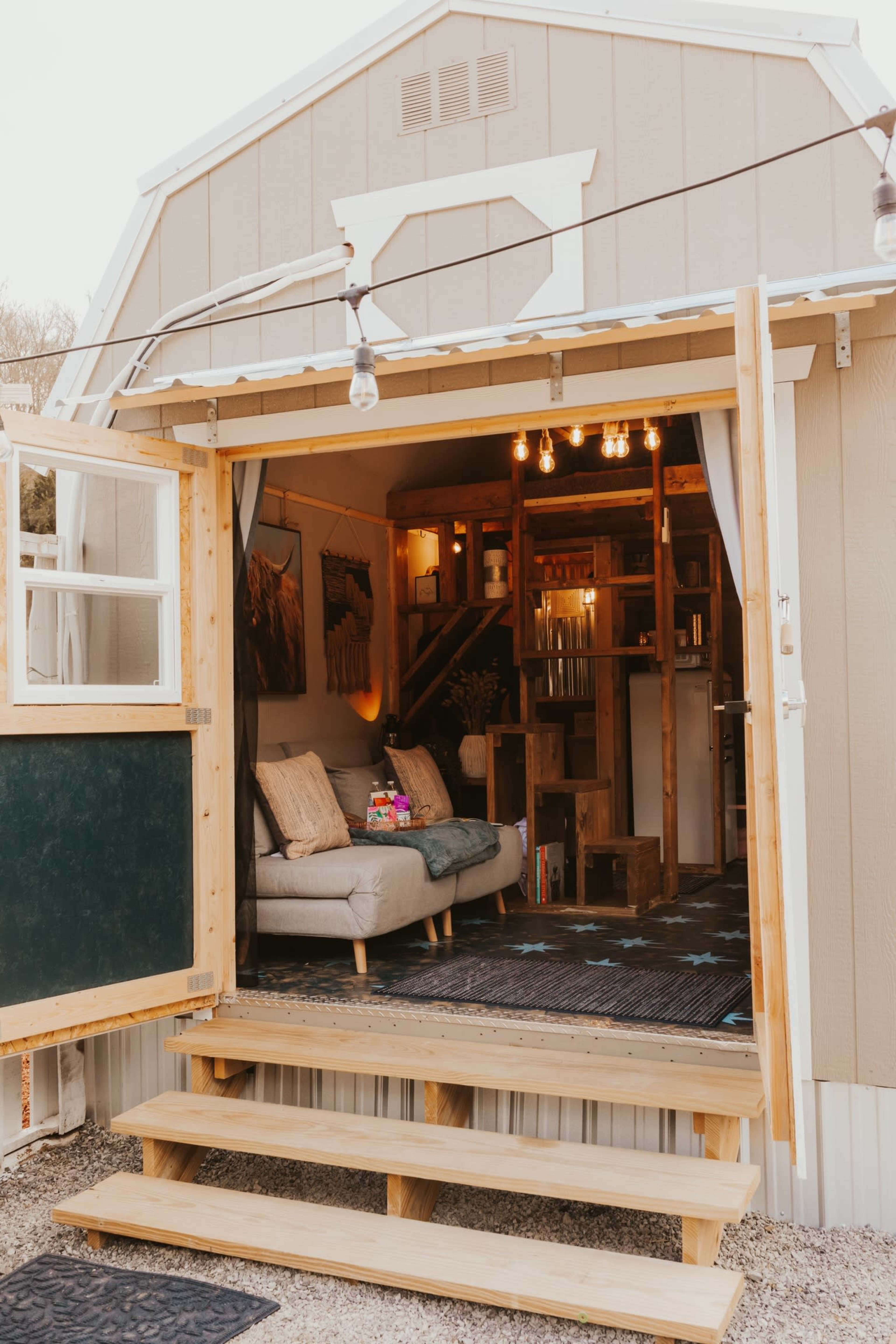 A cozy living space with a sofa and warm lighting is visible through an open barn-style door, leading to wooden steps.