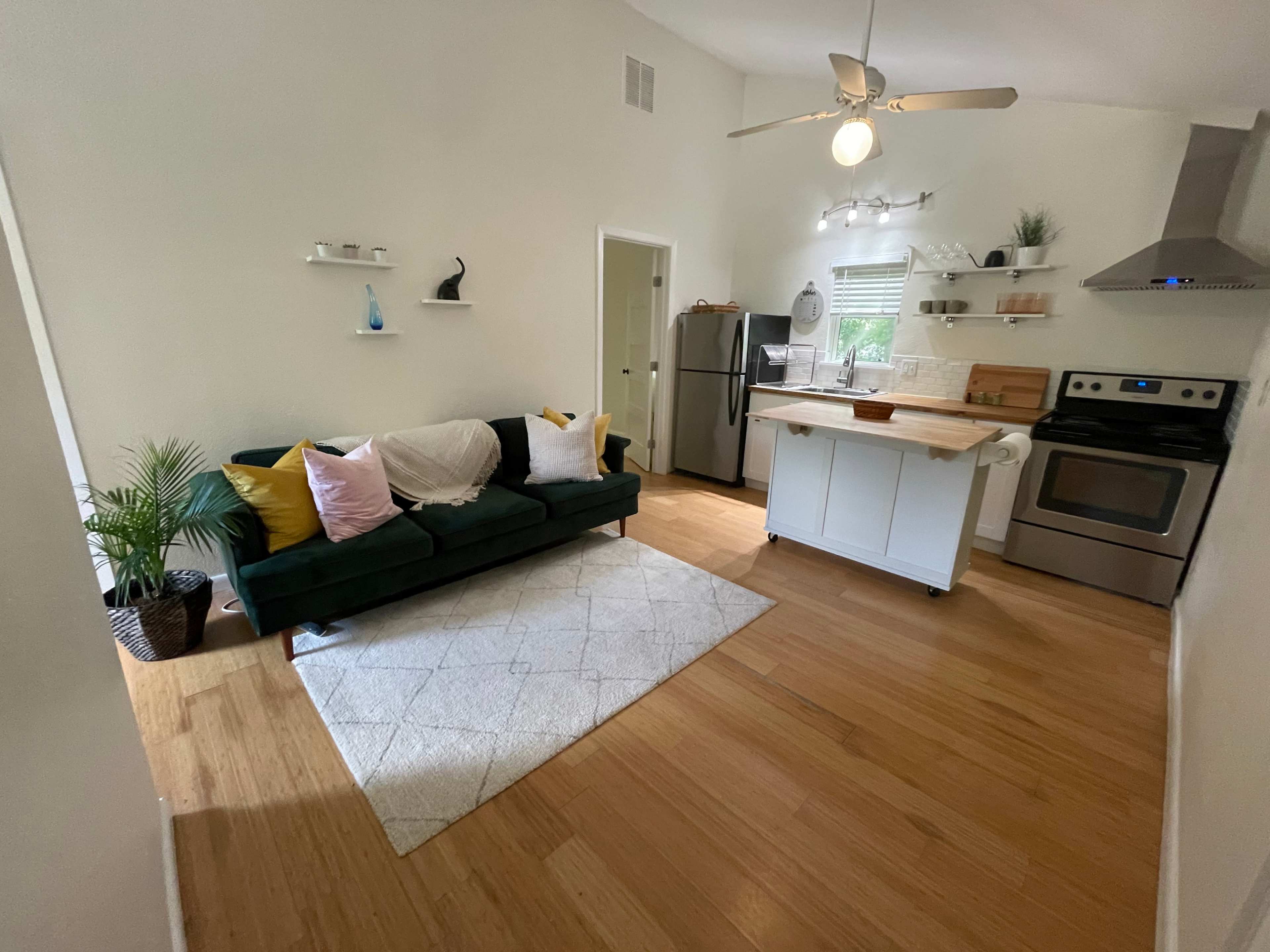 A compact kitchen and living area featuring a green couch, a small dining table, and modern appliances with a wooden countertop.