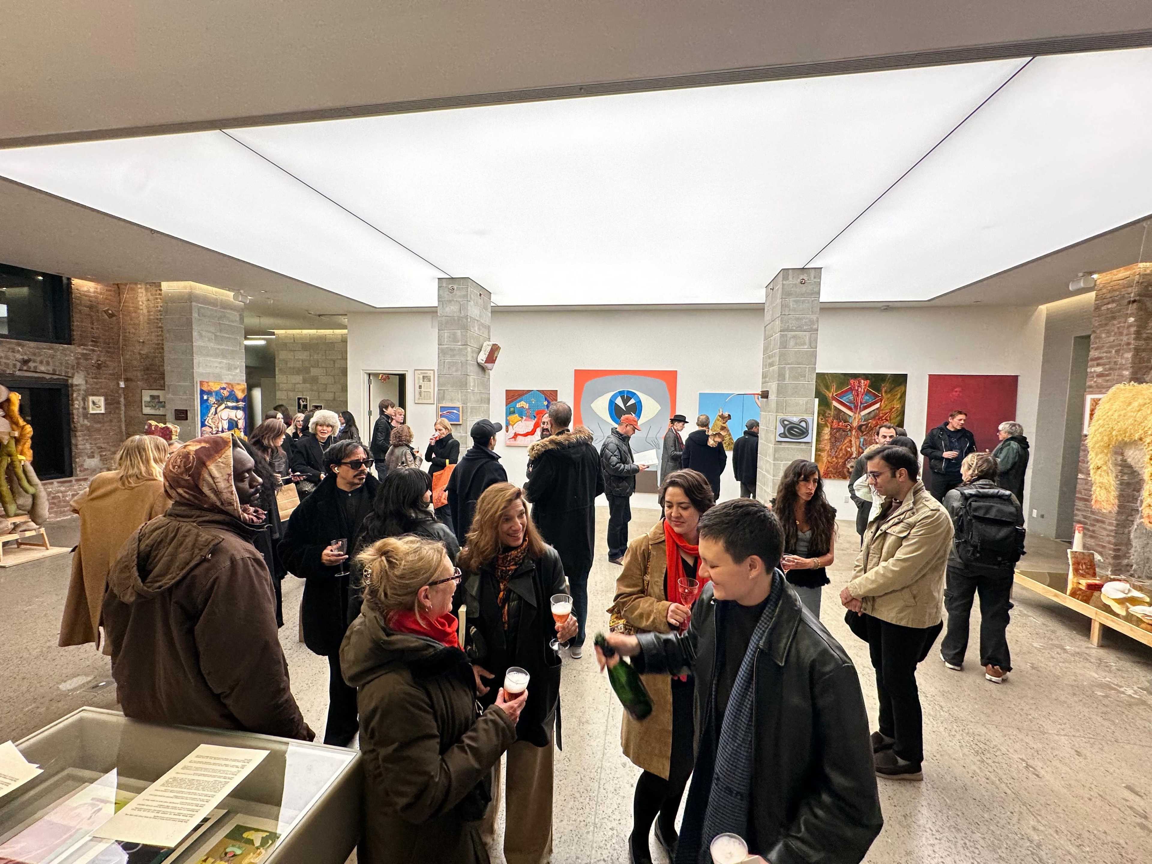 A crowd of people gathers in a spacious art gallery, engaging in conversation while surrounded by various artworks displayed on the walls.