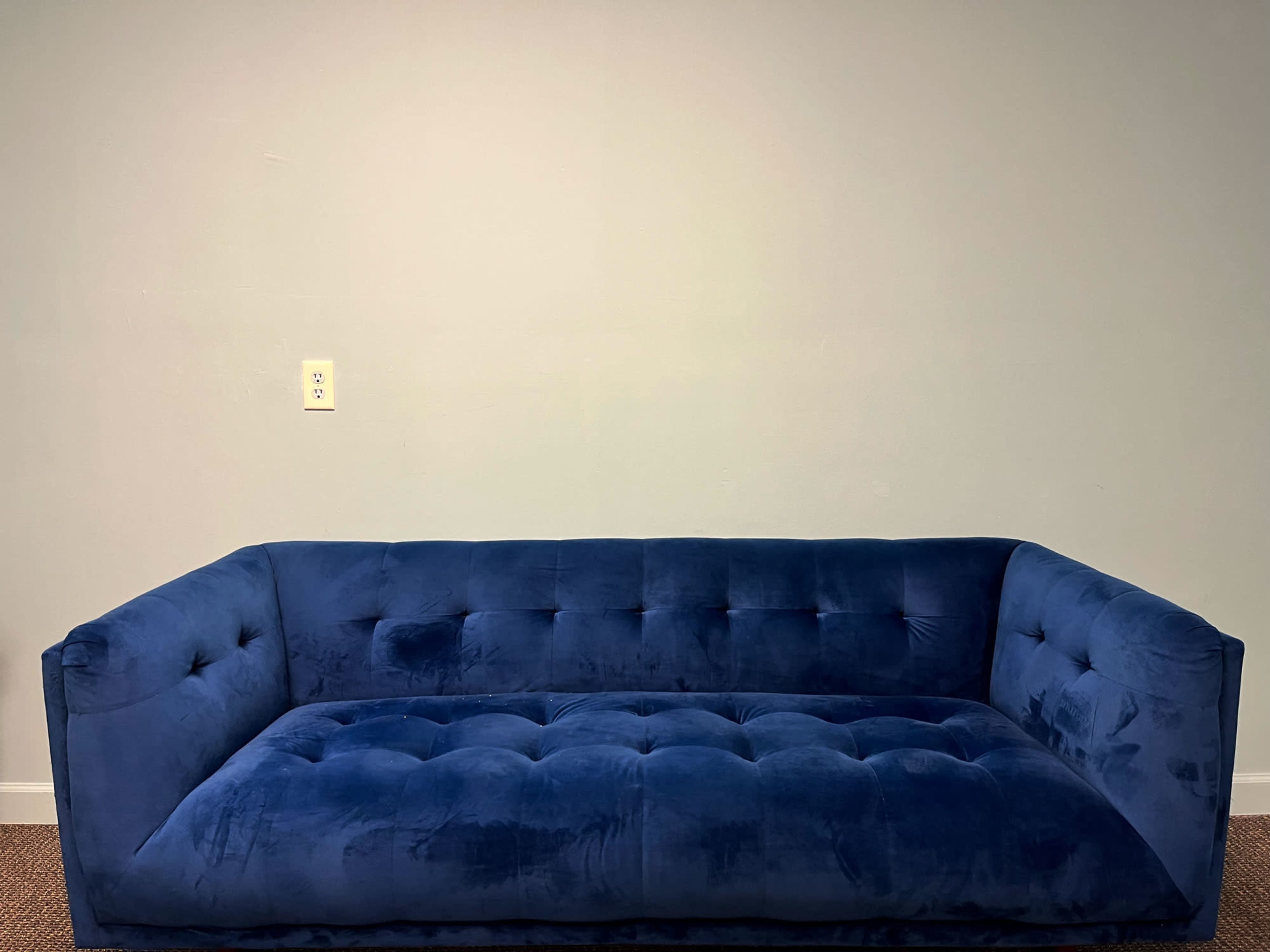 A blue velvet sofa with tufted cushions is positioned against a plain wall.