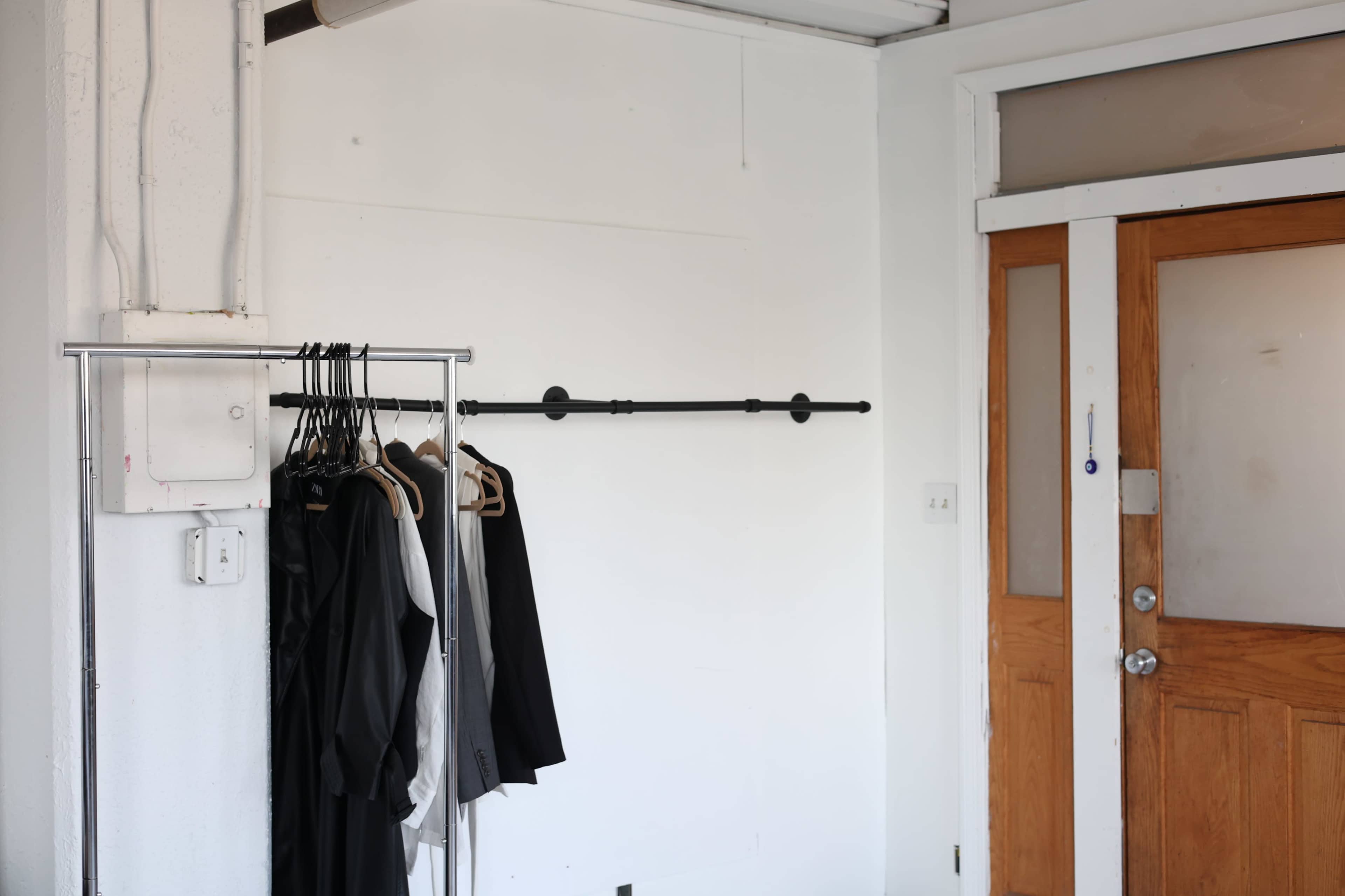 A clothing rack with several garments hangs against a white wall near a wooden door.