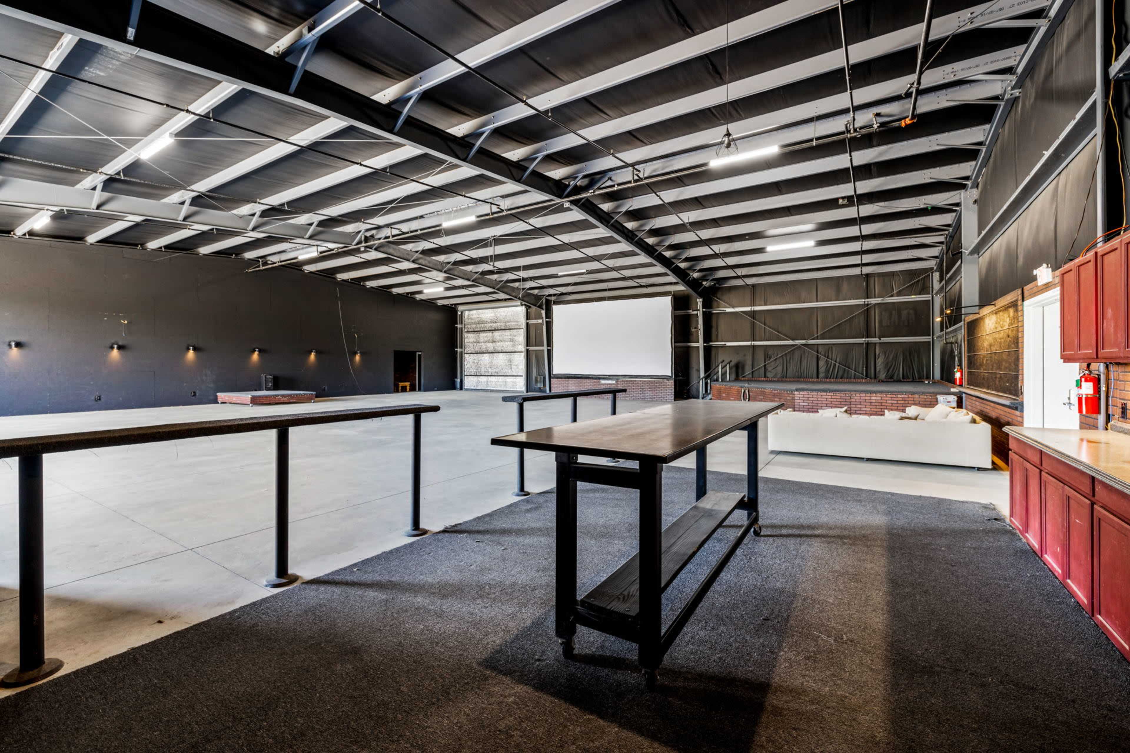 A spacious interior of a commercial building with exposed metal beams, a concrete floor, and a bar-style table in the foreground.
