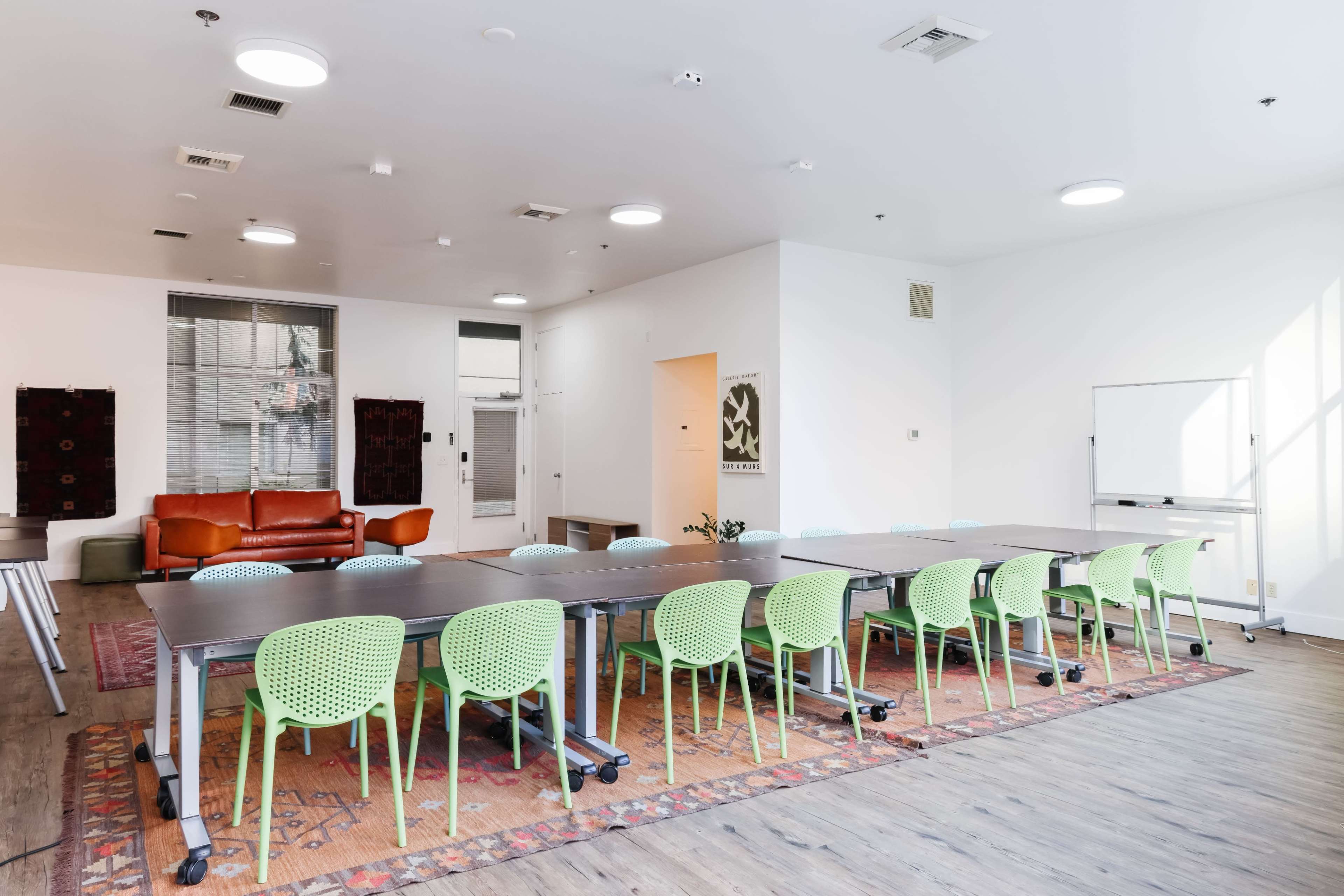 A spacious meeting room features a long table with green chairs, a brown sofa, and large windows allowing natural light.