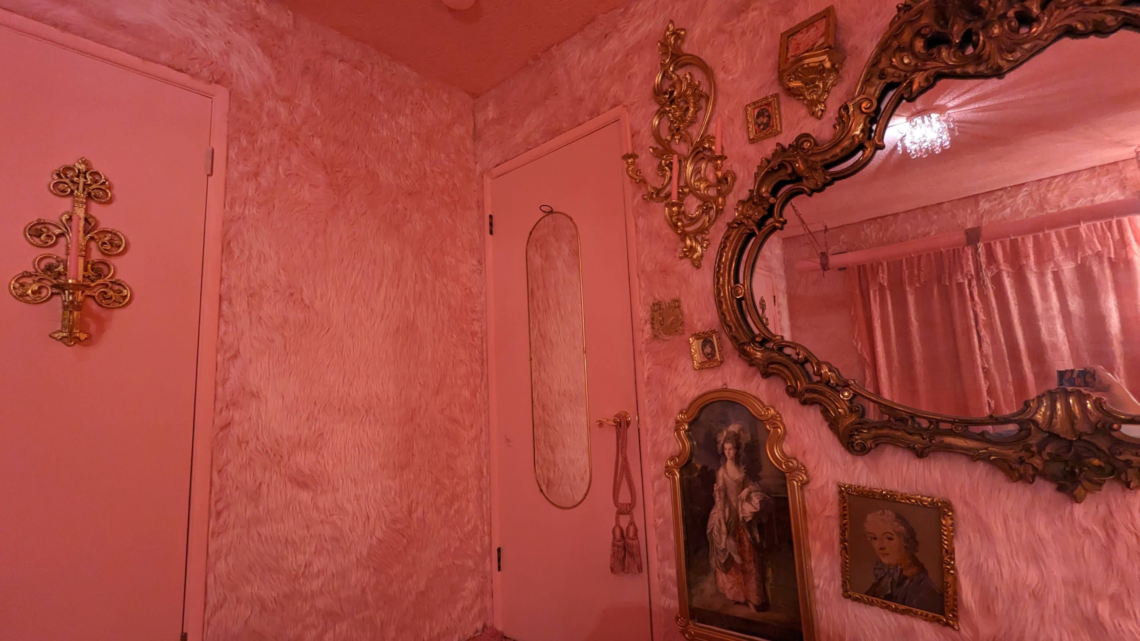 A room featuring pink textured walls, a pink door, and decorative gold-framed mirrors and artwork.