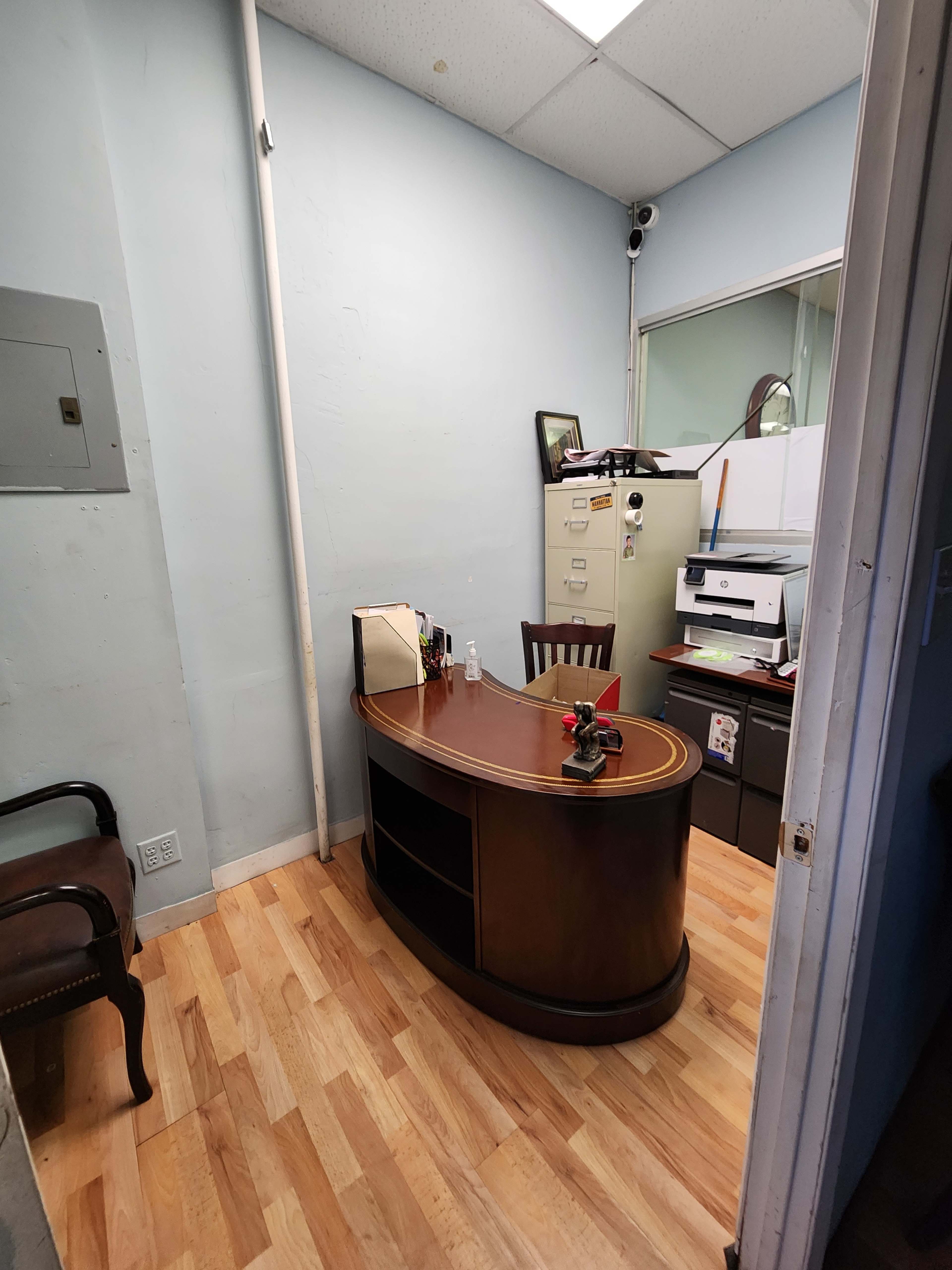 A small office space featuring a curved wooden desk, a chair, filing cabinets, and a printer.