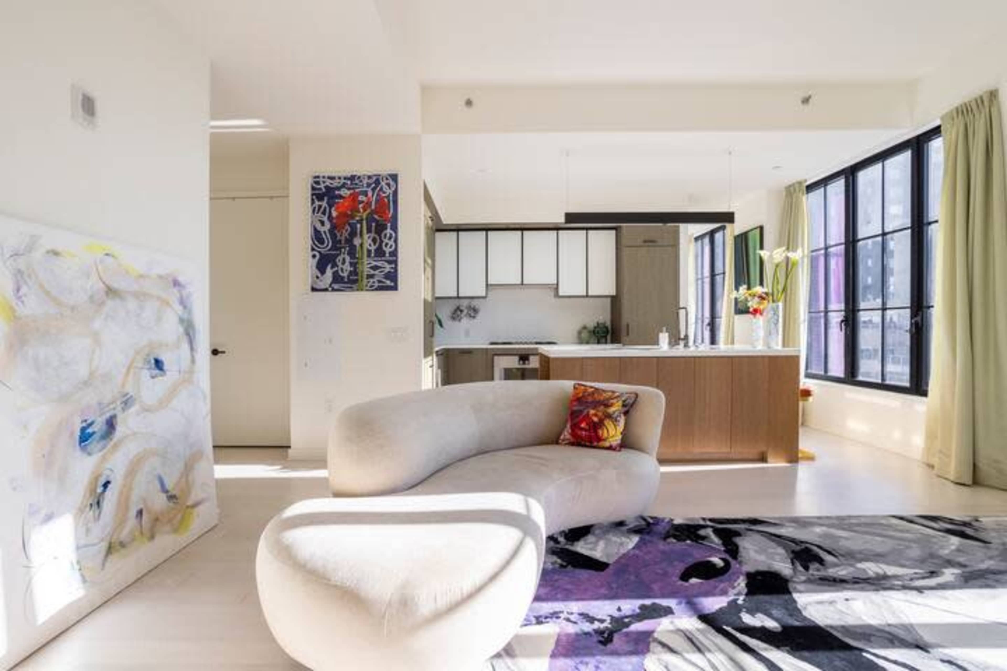 A modern living space features a curved sofa, a colorful area rug, and large windows allowing natural light to enter.