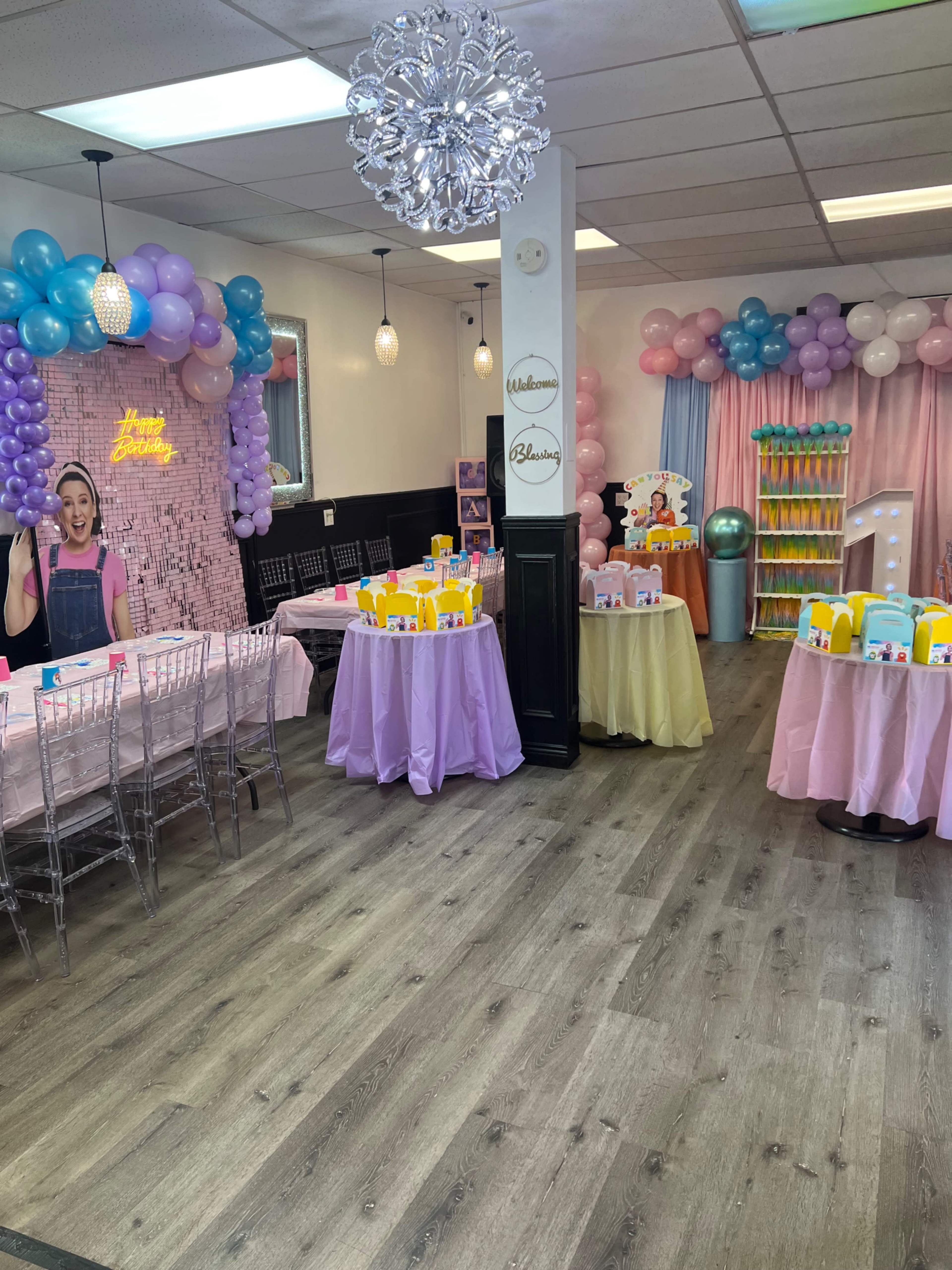 The image shows a vibrant party venue arranged with decorated tables, colorful balloons, and a playful backdrop, designed for a children's celebration.