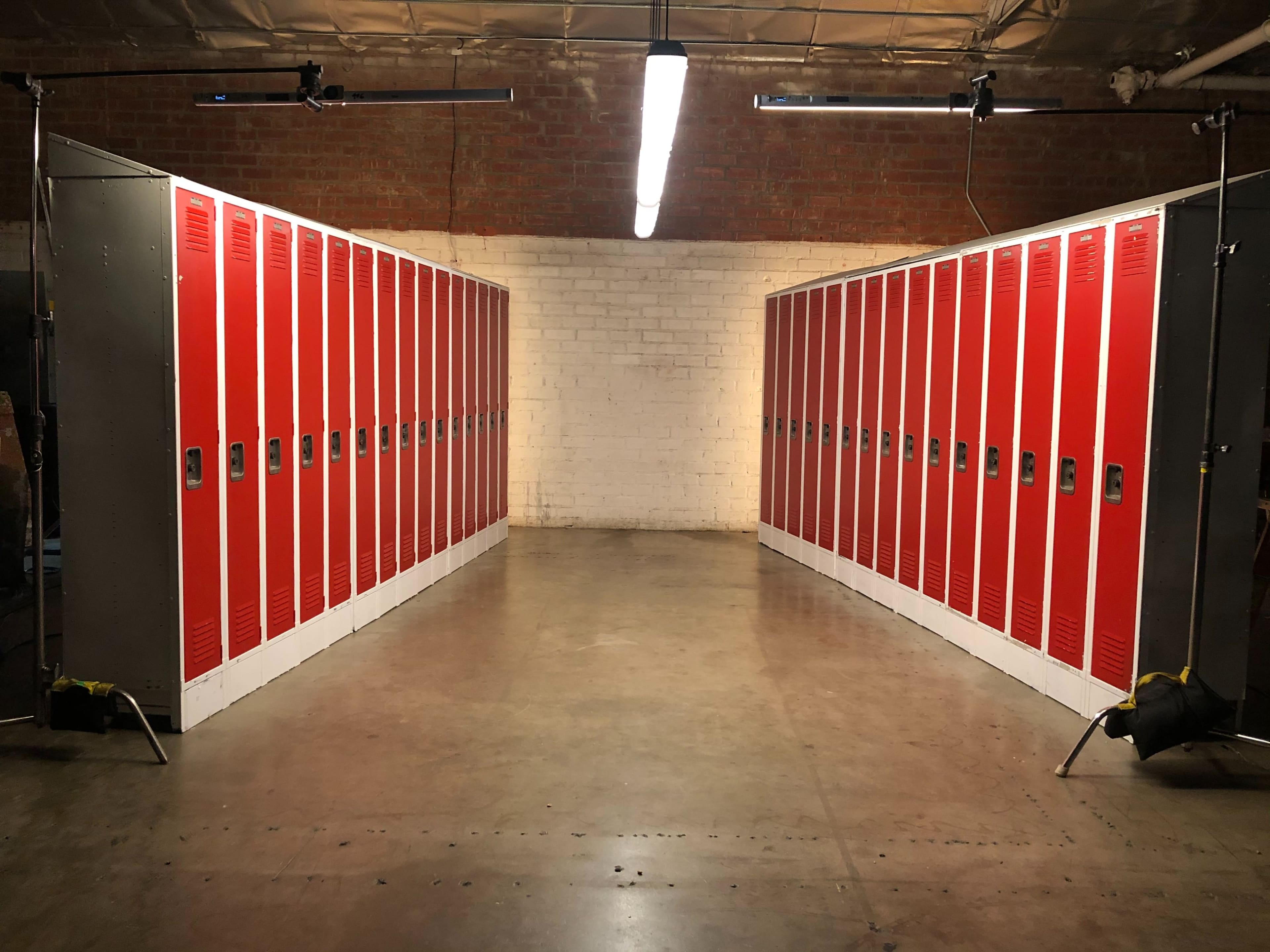 The image shows two rows of red lockers facing each other in a large, industrial space with a concrete floor.