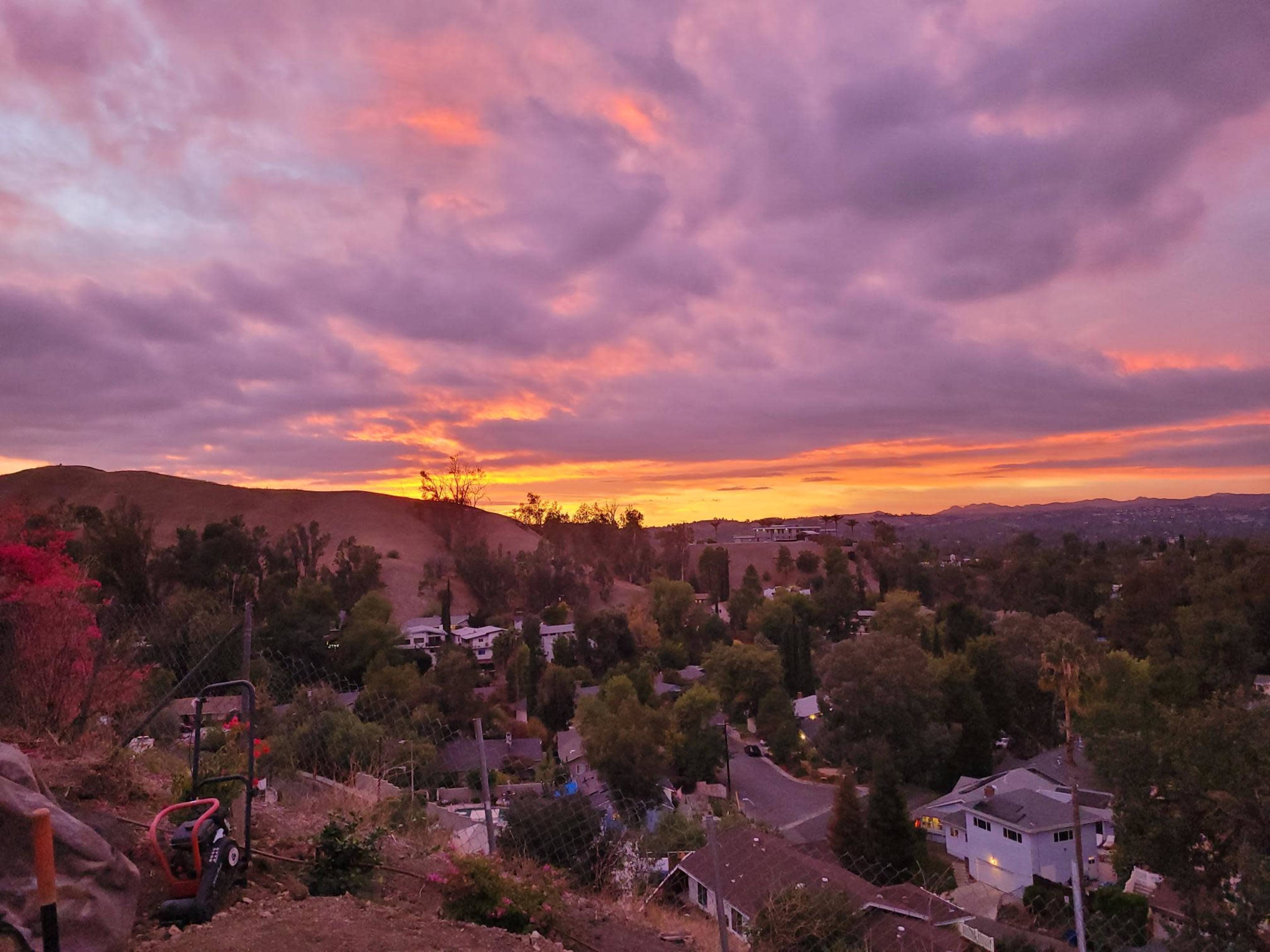 A sunset over a suburban neighborhood with rolling hills in the background.