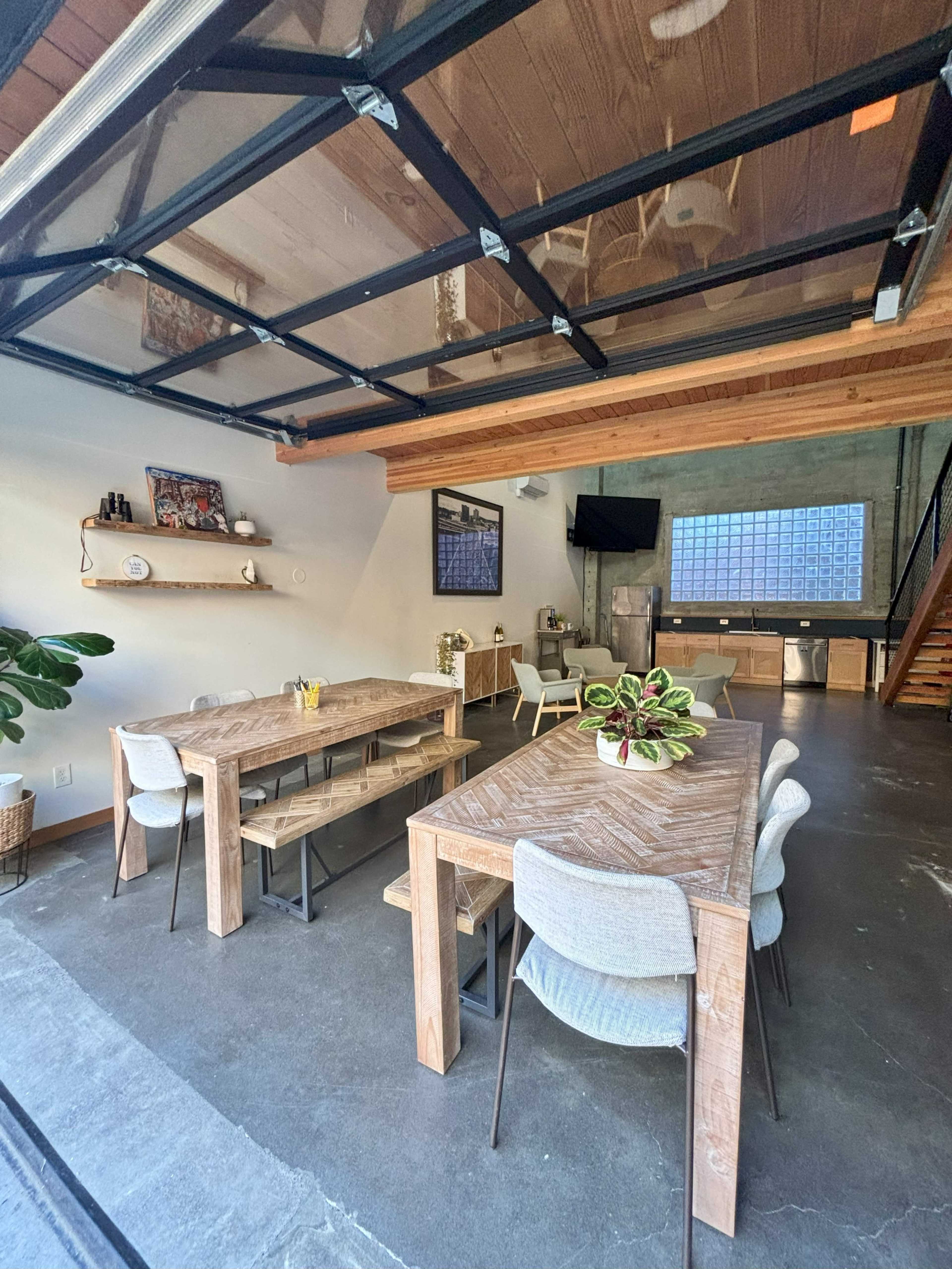 The image shows a spacious dining area with wooden tables, chairs, and an open garage door leading to an outdoor space.