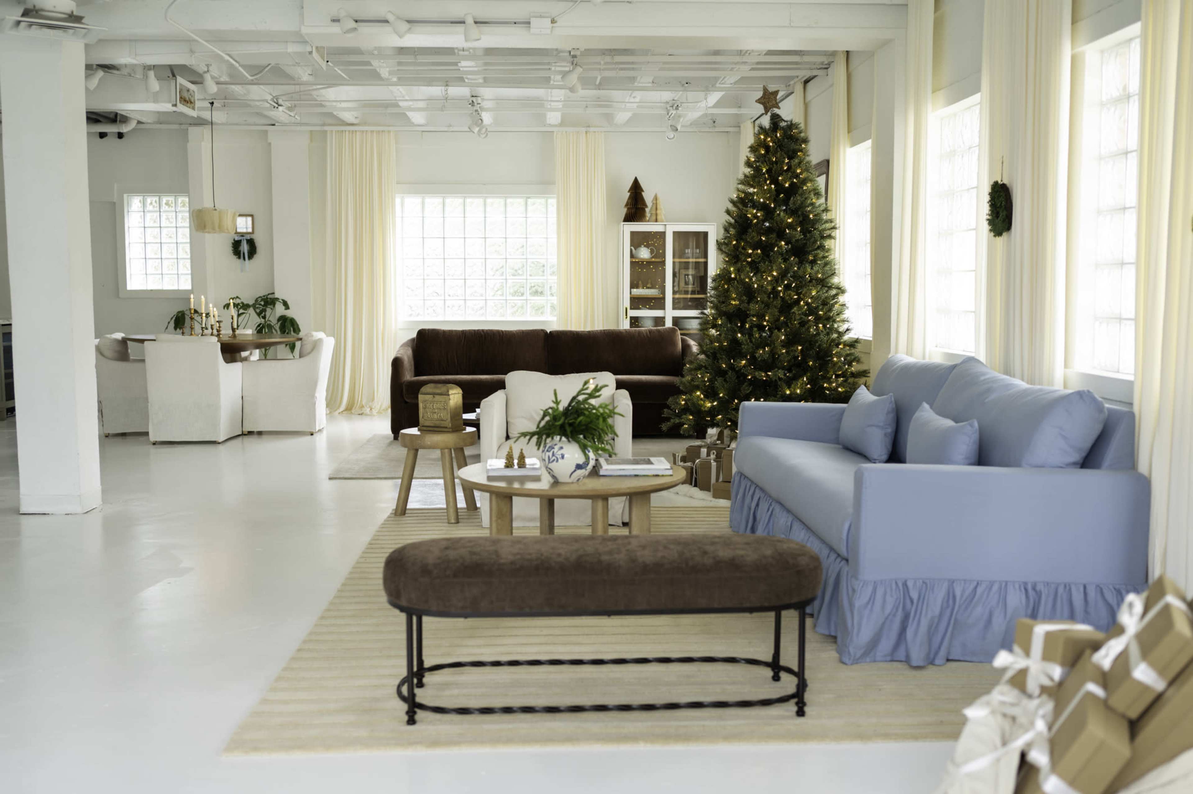 The bright and spacious room features a decorated Christmas tree, various seating arrangements, and light-colored walls.