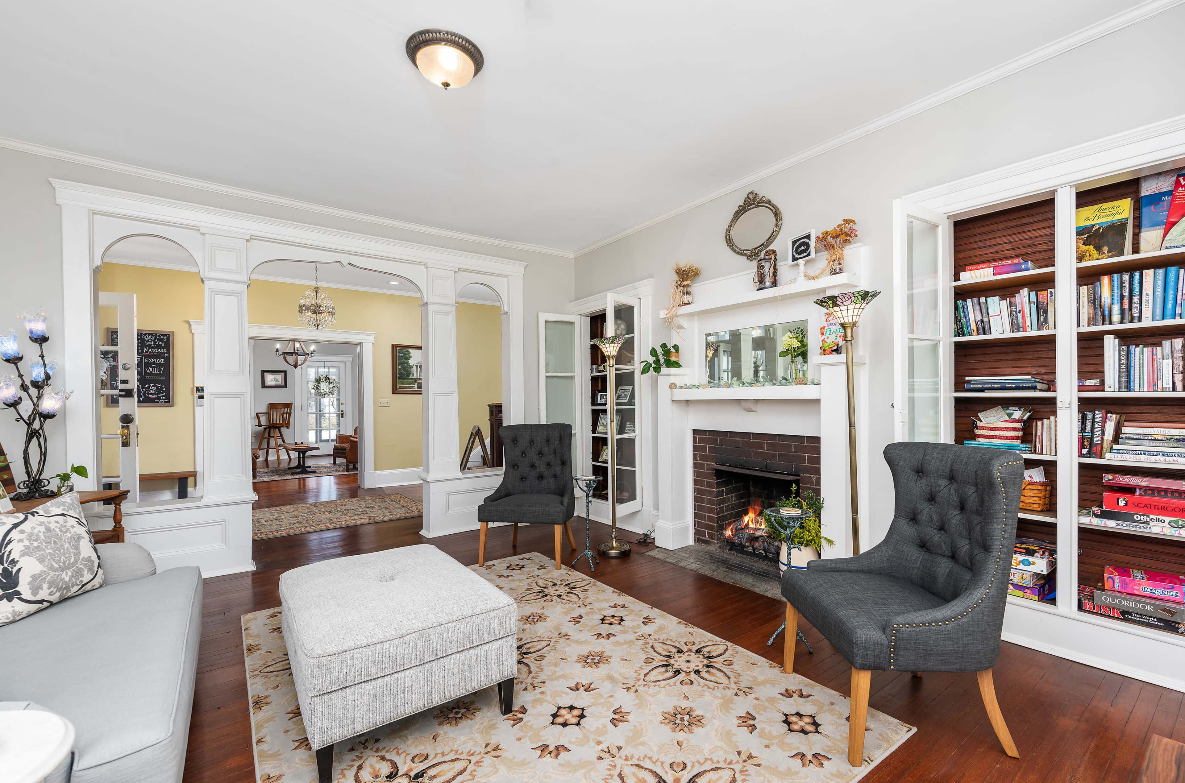 The living room features a cozy seating arrangement with two chairs, a central ottoman, and a fireplace surrounded by built-in bookshelves.