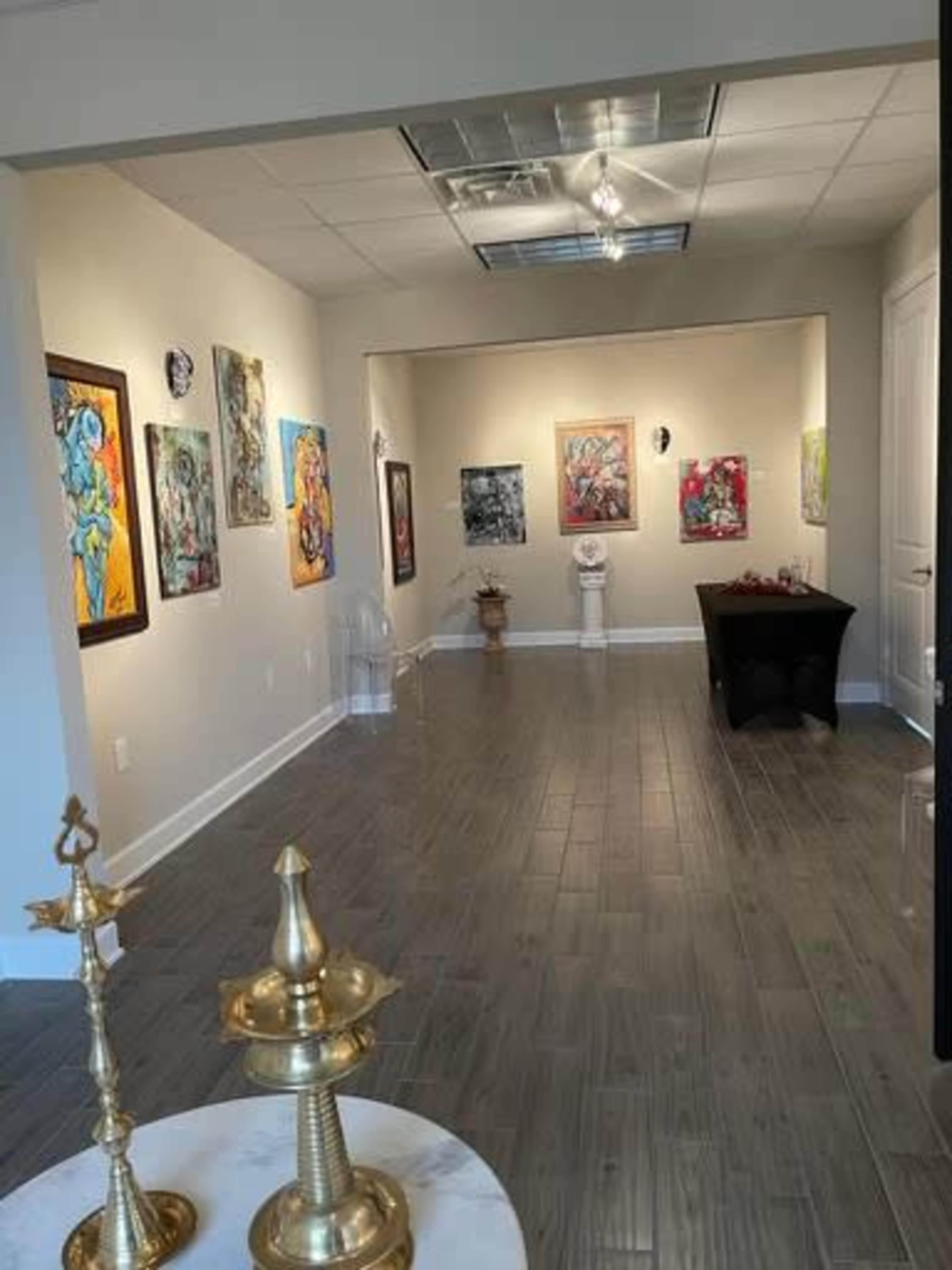 An art gallery with several colorful paintings hanging on the walls, a central display table, and decorative lighting.