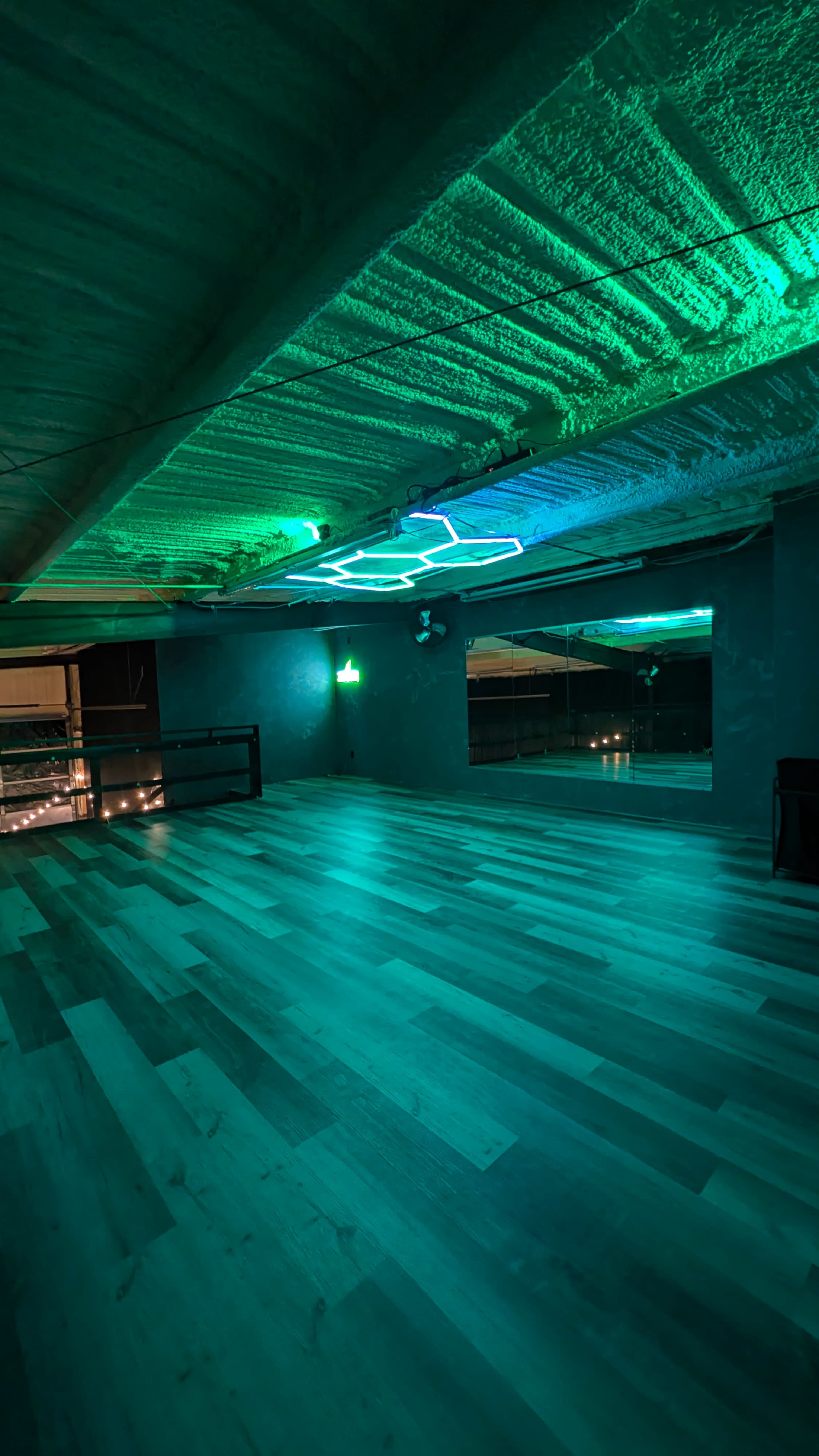The image shows an empty dance studio with green neon lighting and wooden flooring.