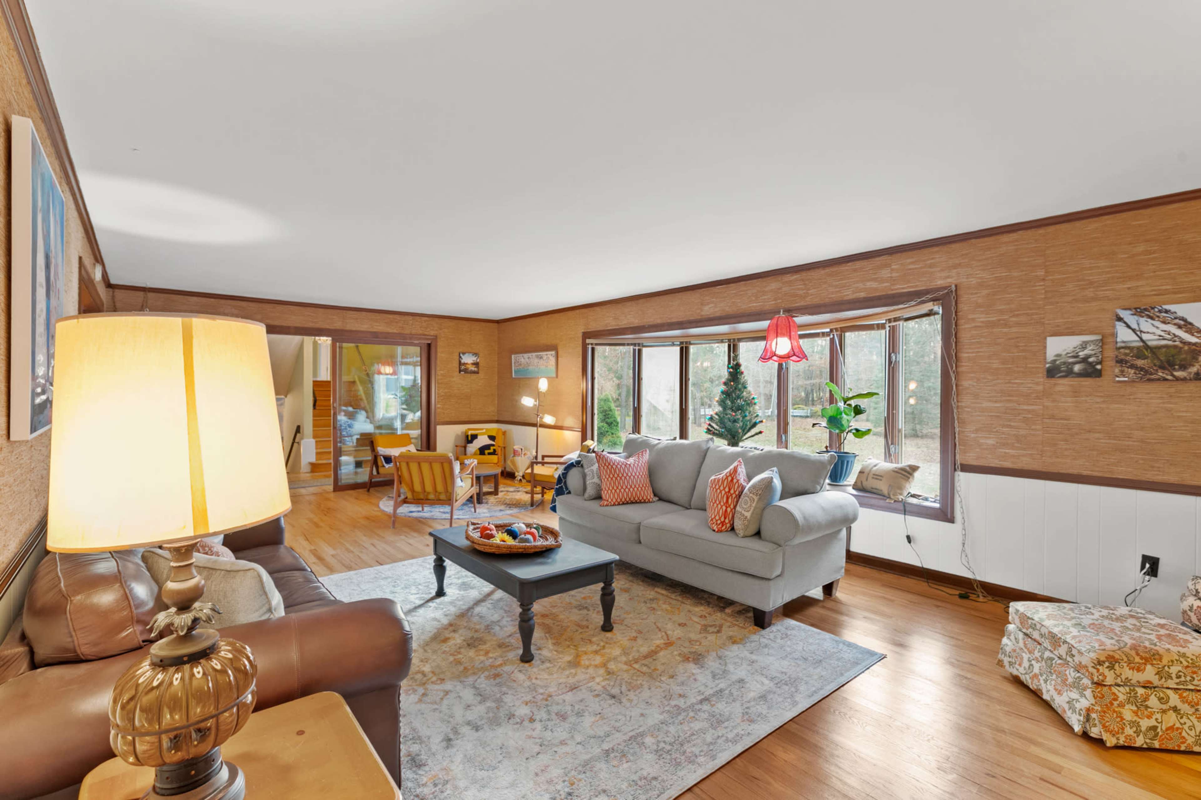 The living room features a gray couch, a brown leather chair, a coffee table with snacks, and large windows that provide natural light.