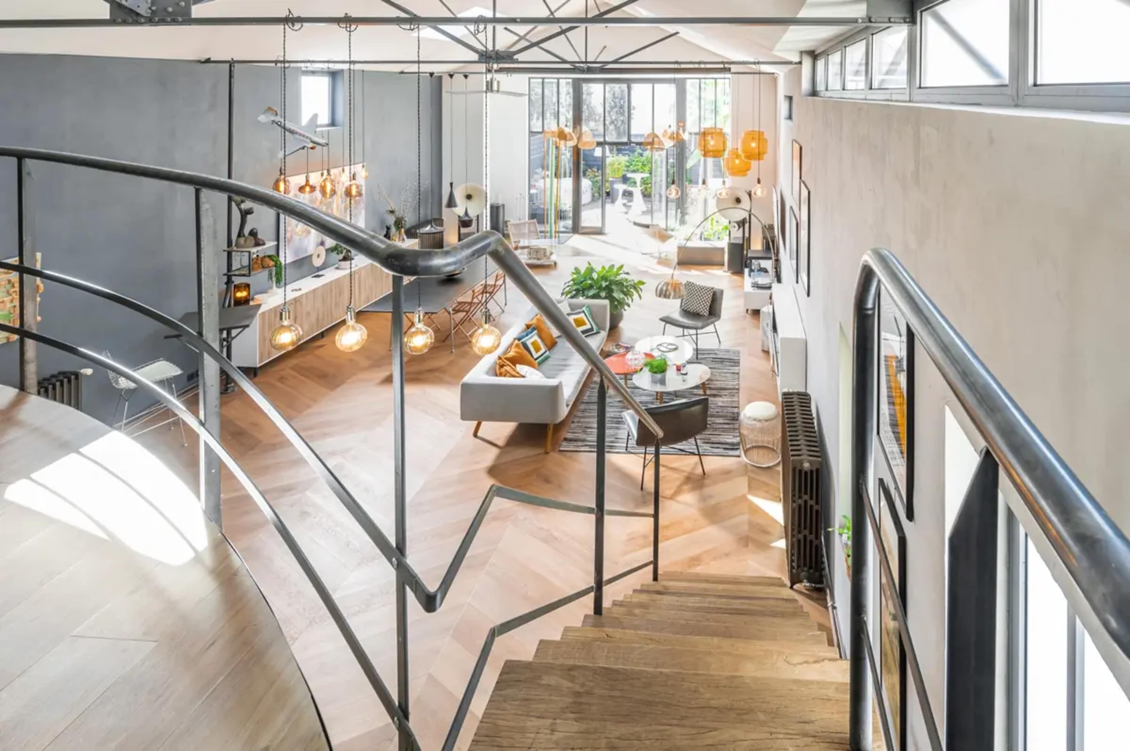 A modern interior space featuring an open layout with a staircase, large windows, and stylish furniture arrangements.